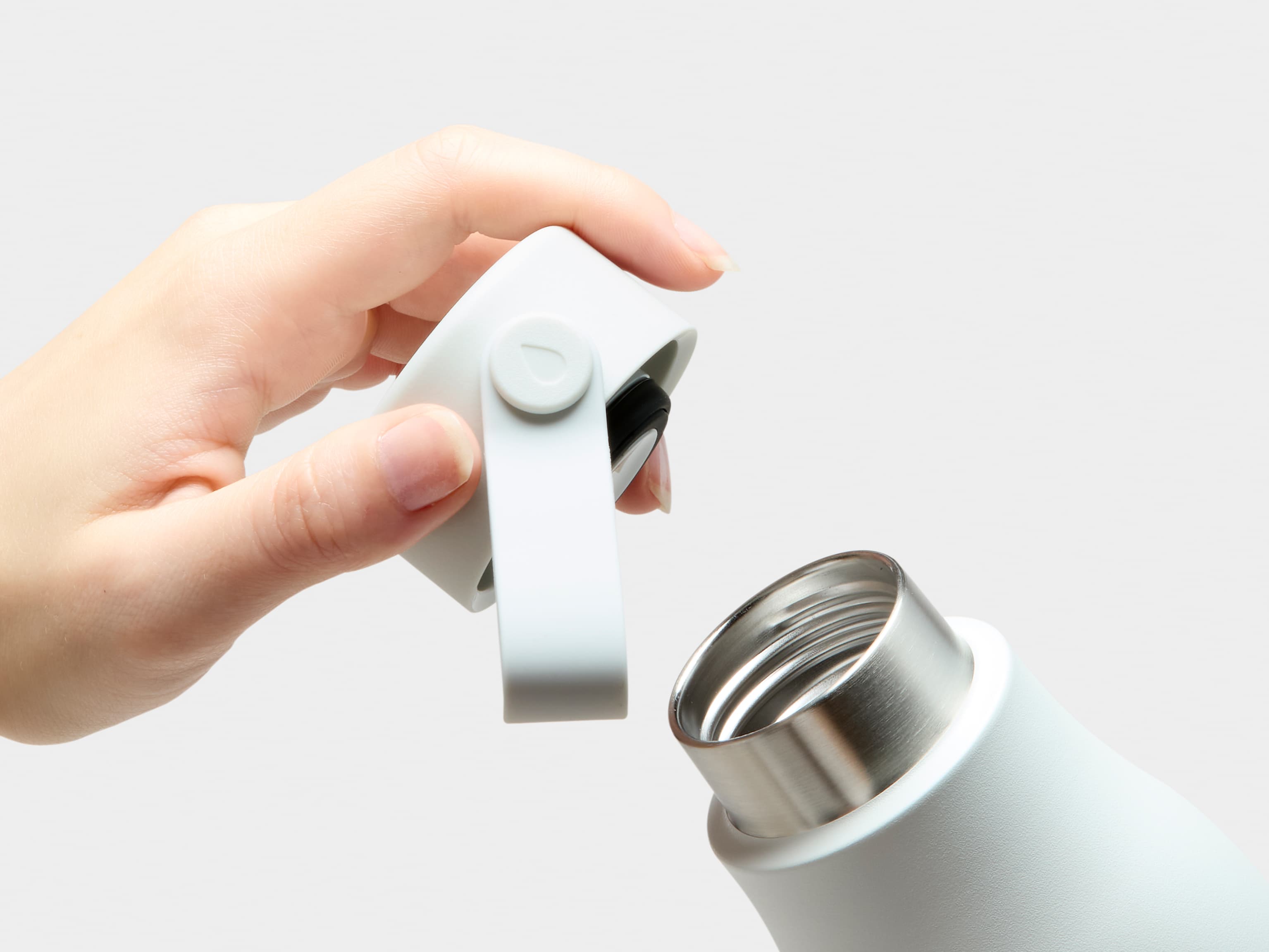 A close up image of the mouth and a hand holding the lid of a cloudy grey MOO water bottle.