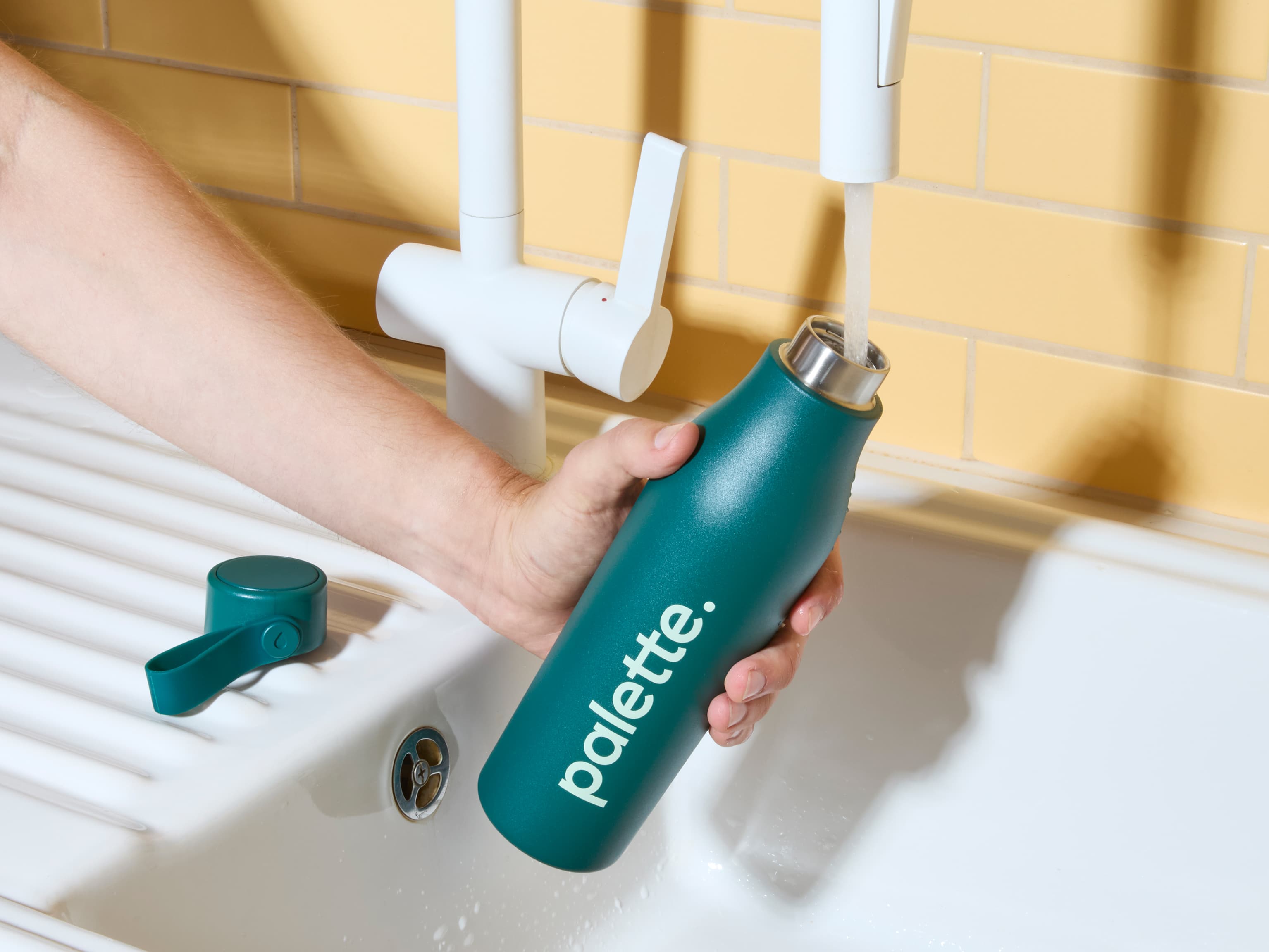 A person filling up a custom green water bottle from a tap.