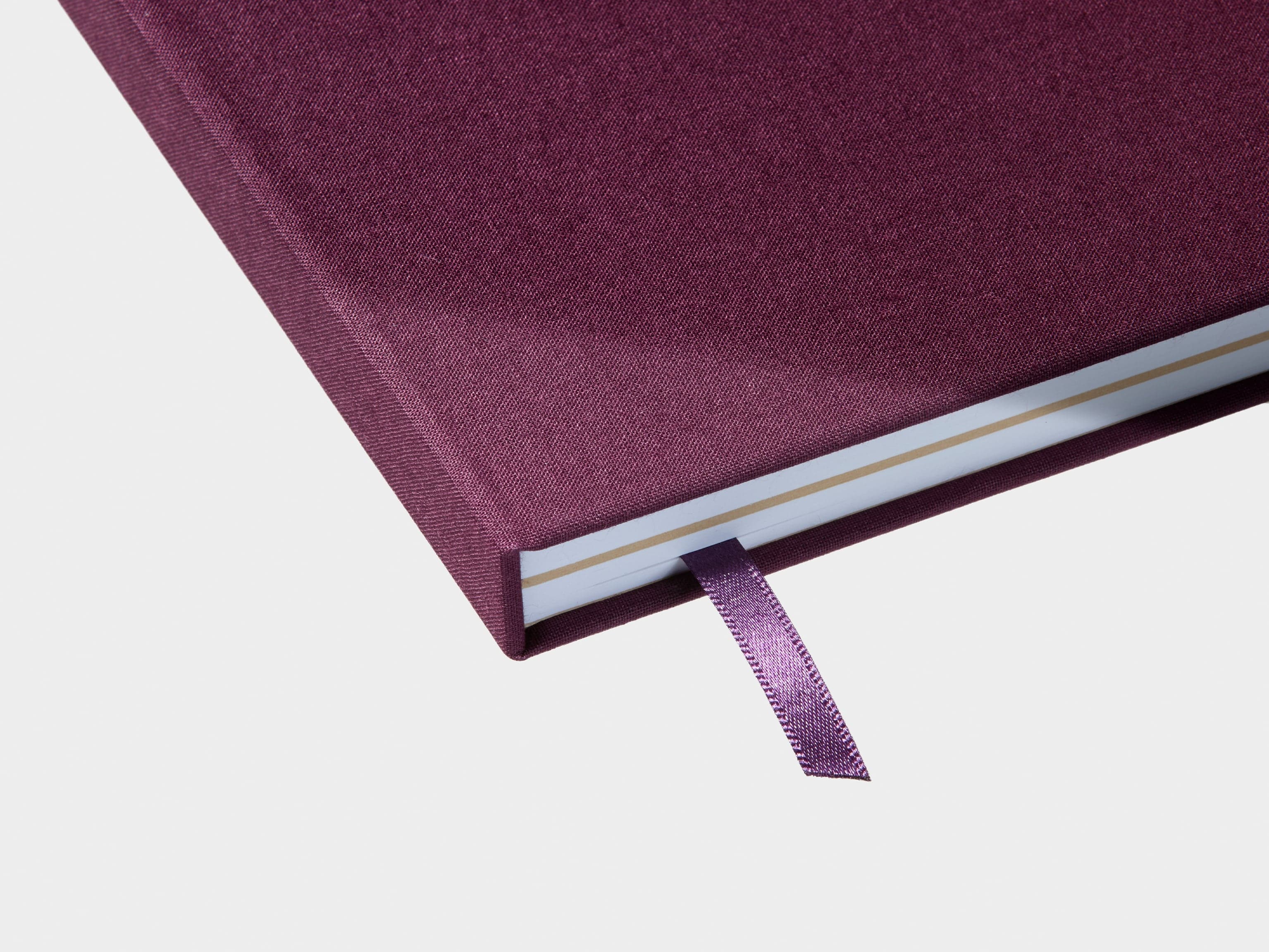 A detail image of the bottom corner of a mulberry hardcover notebook closed with a ribbon page marker.