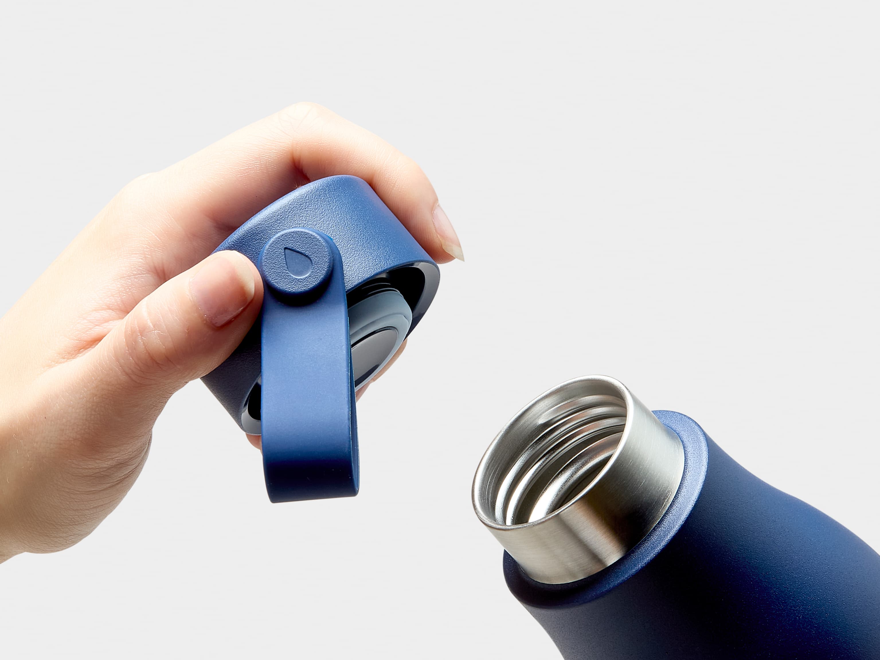 A close up image of the mouth and a hand holding the lid of a midnight blue MOO water bottle.