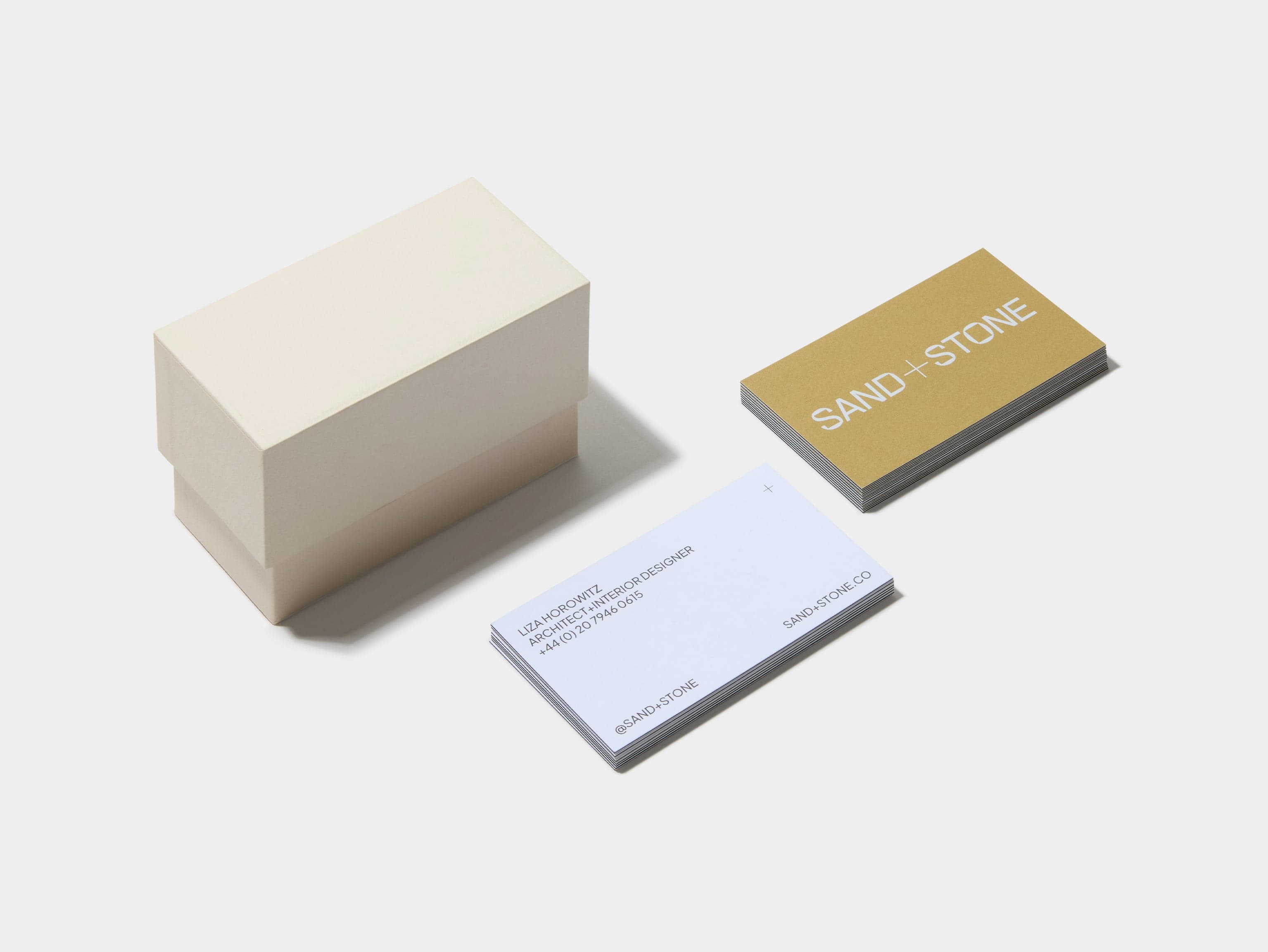 An off white business card box placed alongside two piles of custom luxe business cards.