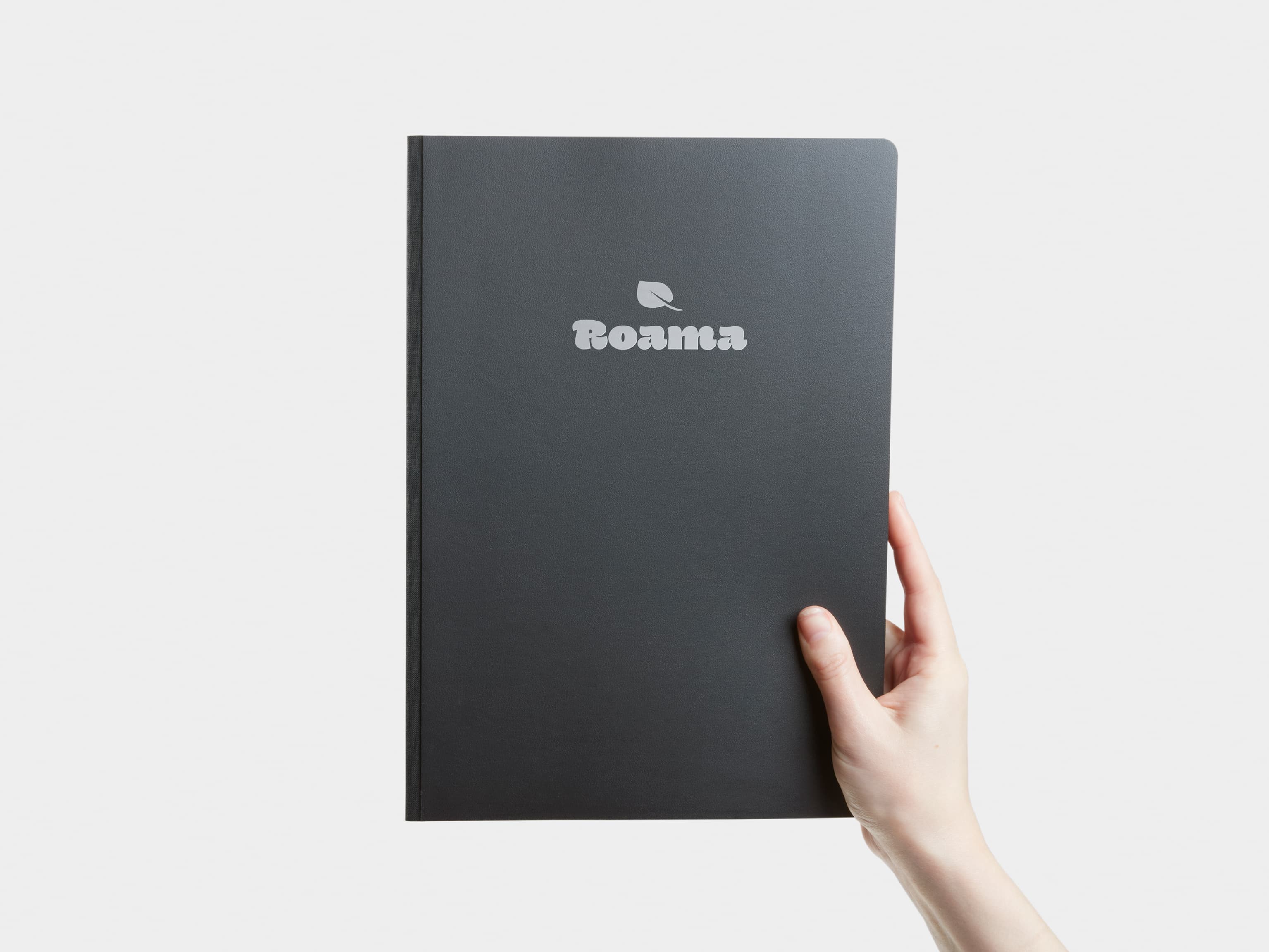 A hand holding a large jet black softcover notebook with silver foil customisation.