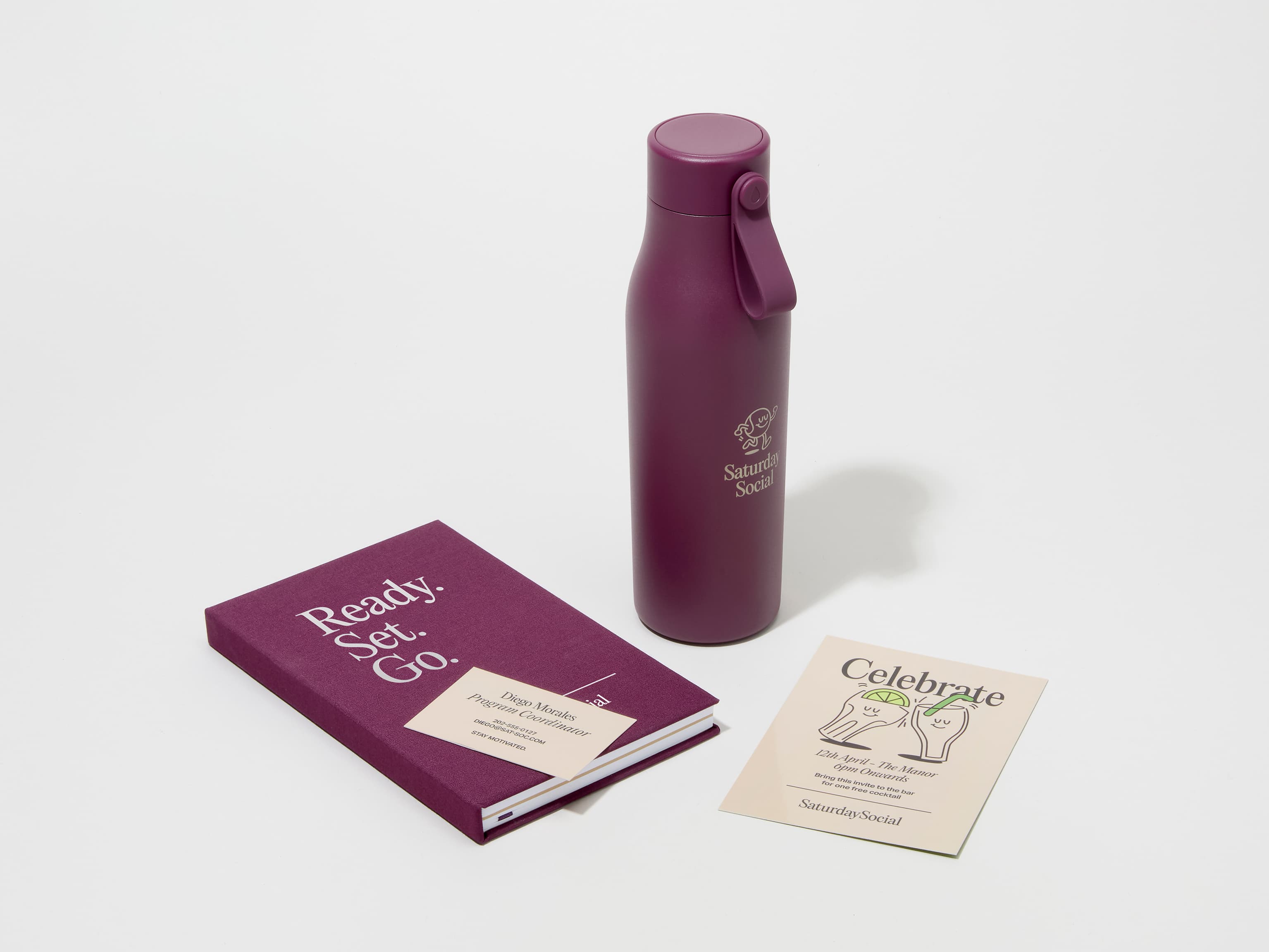 A collection of branded merchandise including a mulberry MOO water bottle with customized engraving alongside a notepad, notebook and pen.