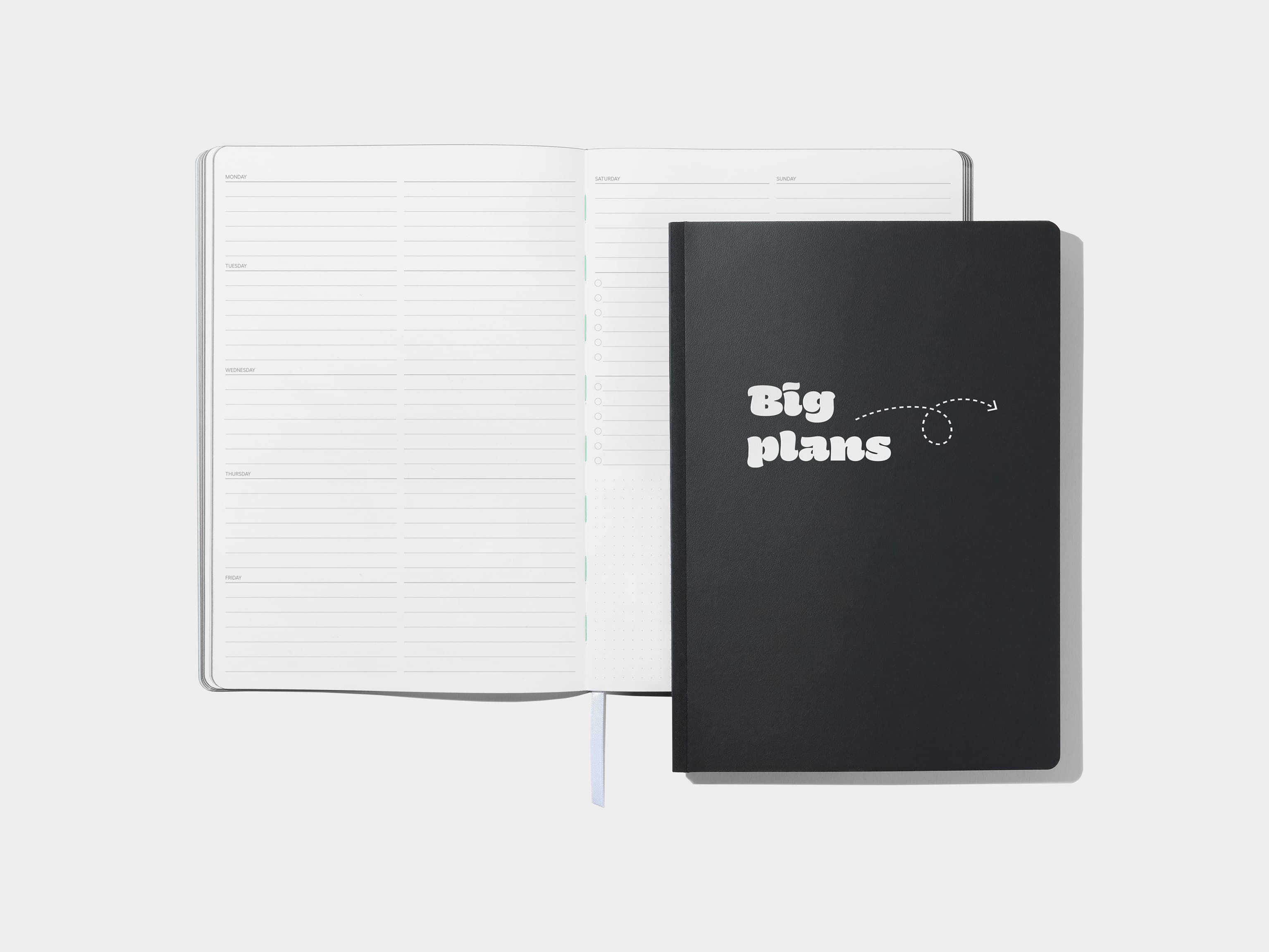 An open softcover planner with lined pages with a jet black softcover planner positioned over the right page.