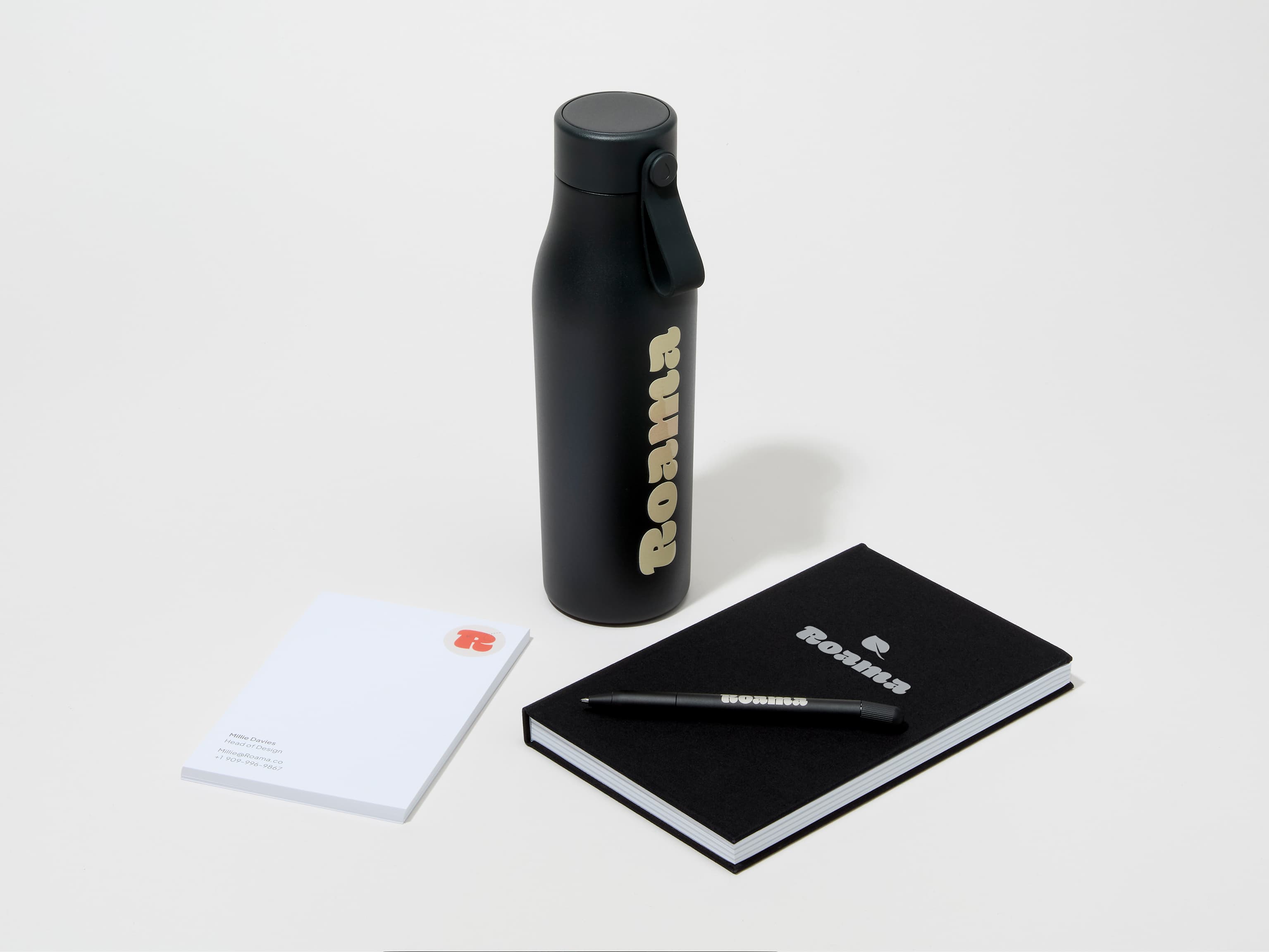 A collection of branded merchandise including a jet black MOO water bottle with customized printing alongside a notepad, notebook and pen.