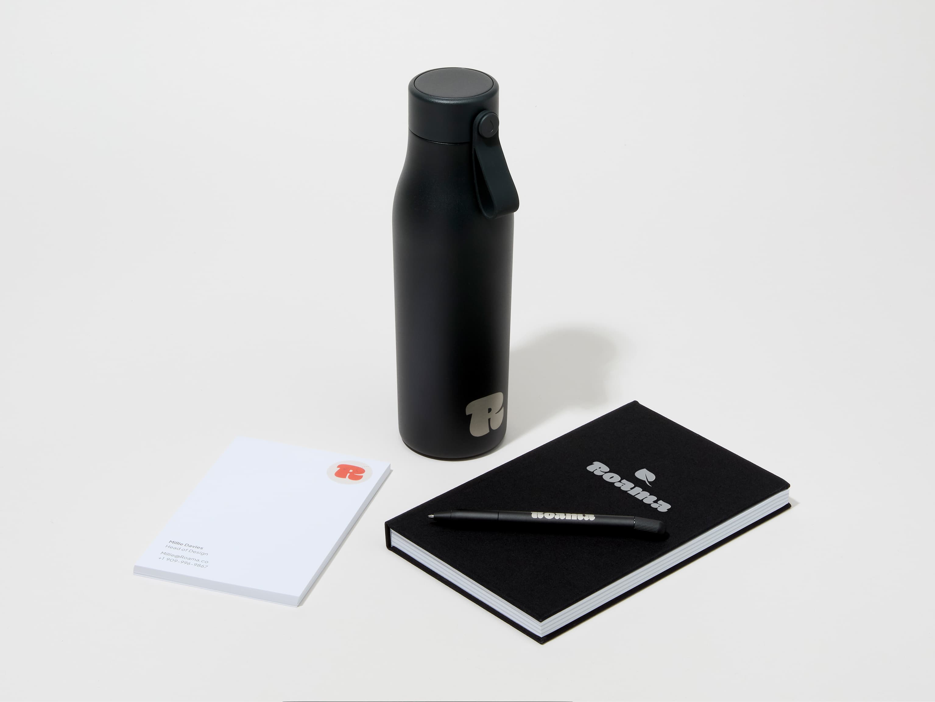 A collection of branded merchandise including a jet black MOO water bottle with customized engraving alongside a notepad, notebook and pen.