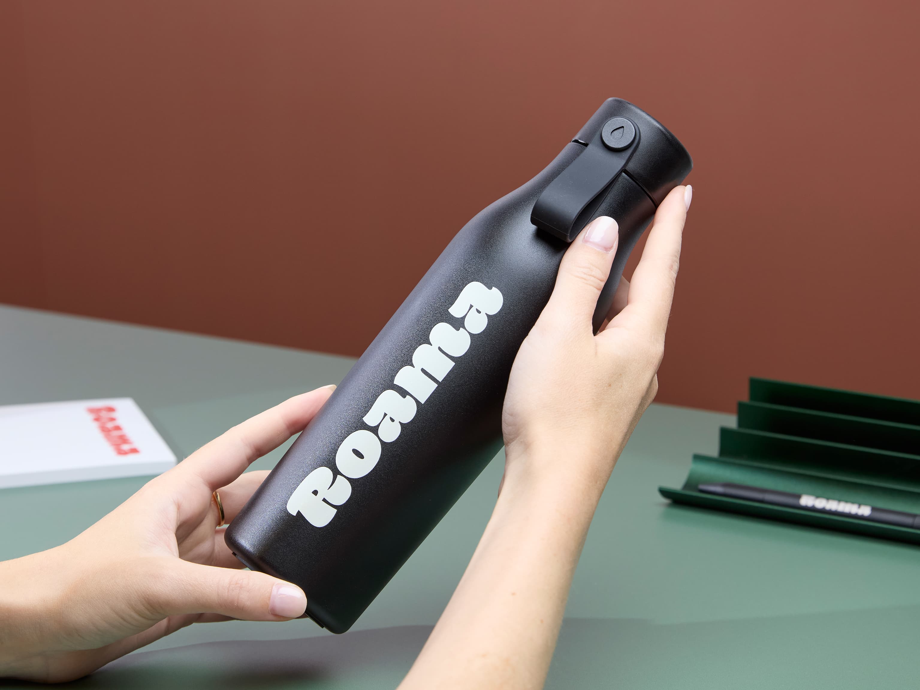 A person holding a jet black water bottle with white custom branding.