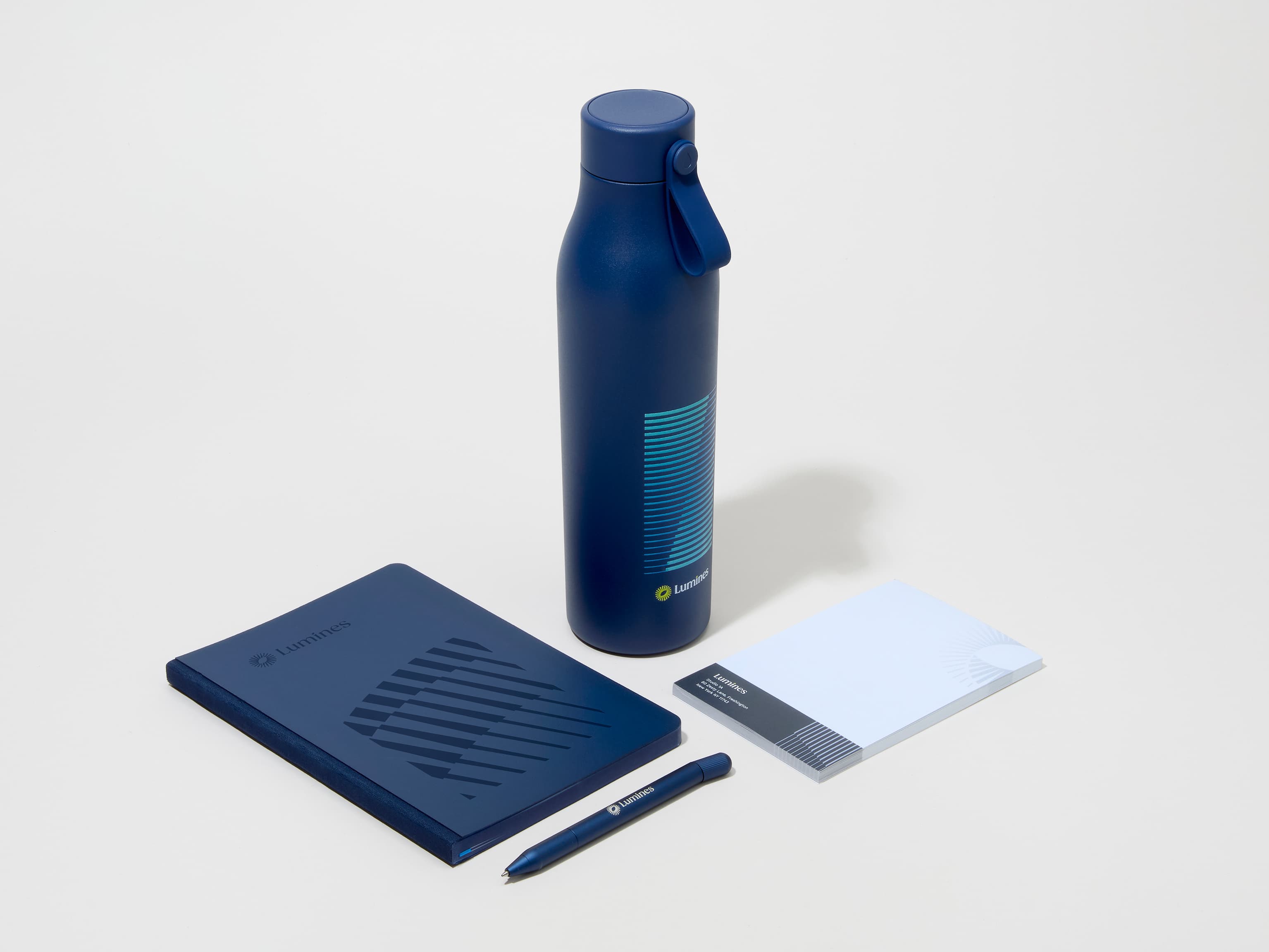 A collection image of a midnight blue MOO water bottle with custom printing alongside a notebook, notepad and pen.