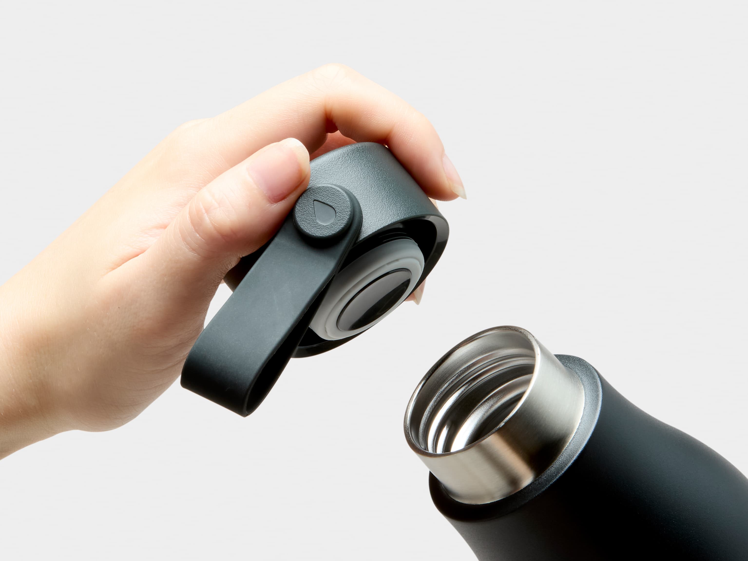 A close up image of the mouth and a hand holding the lid of a jet black MOO water bottle.