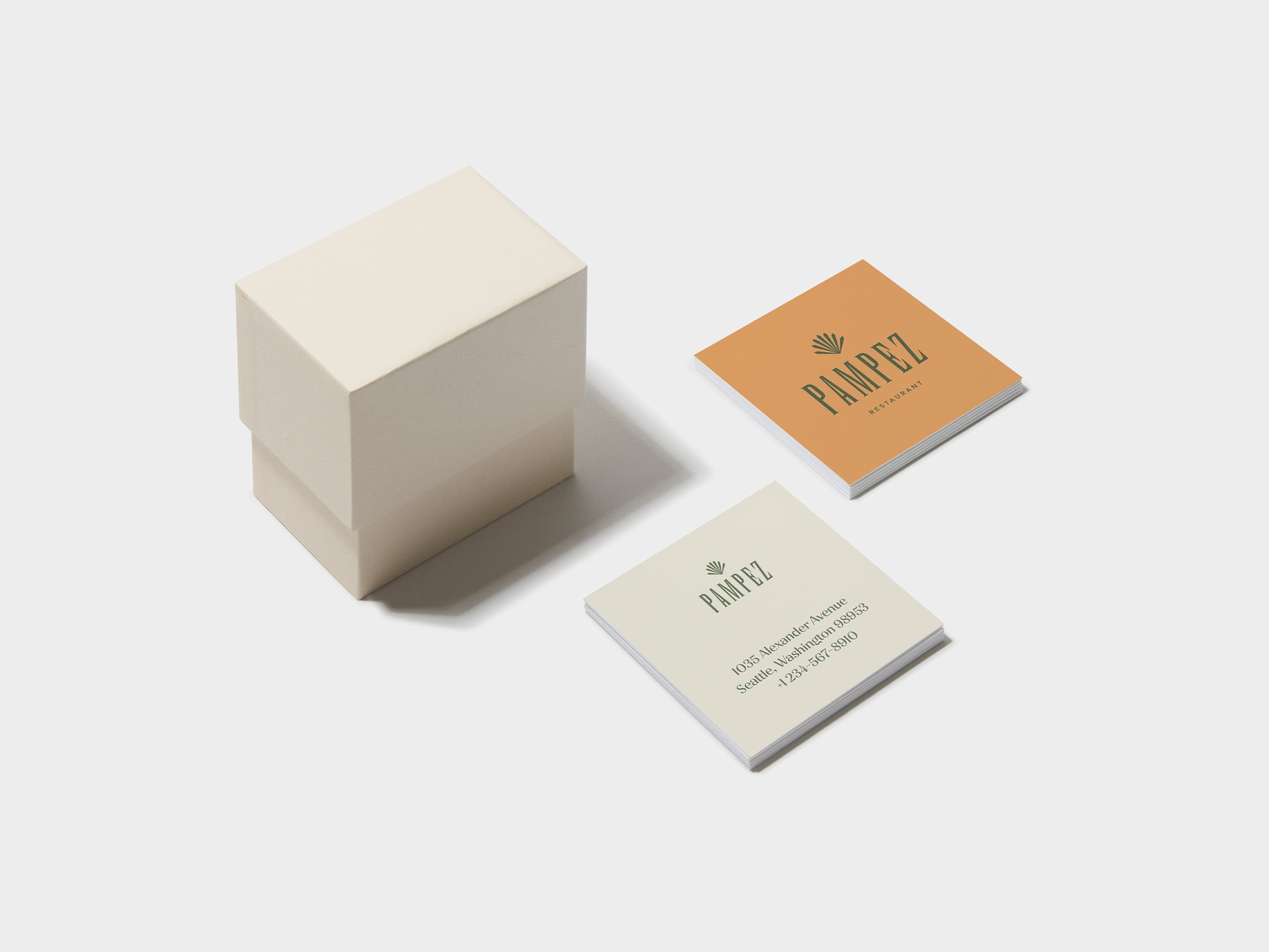 A square off white business card box with two piles of customised business cards placed alongside it.