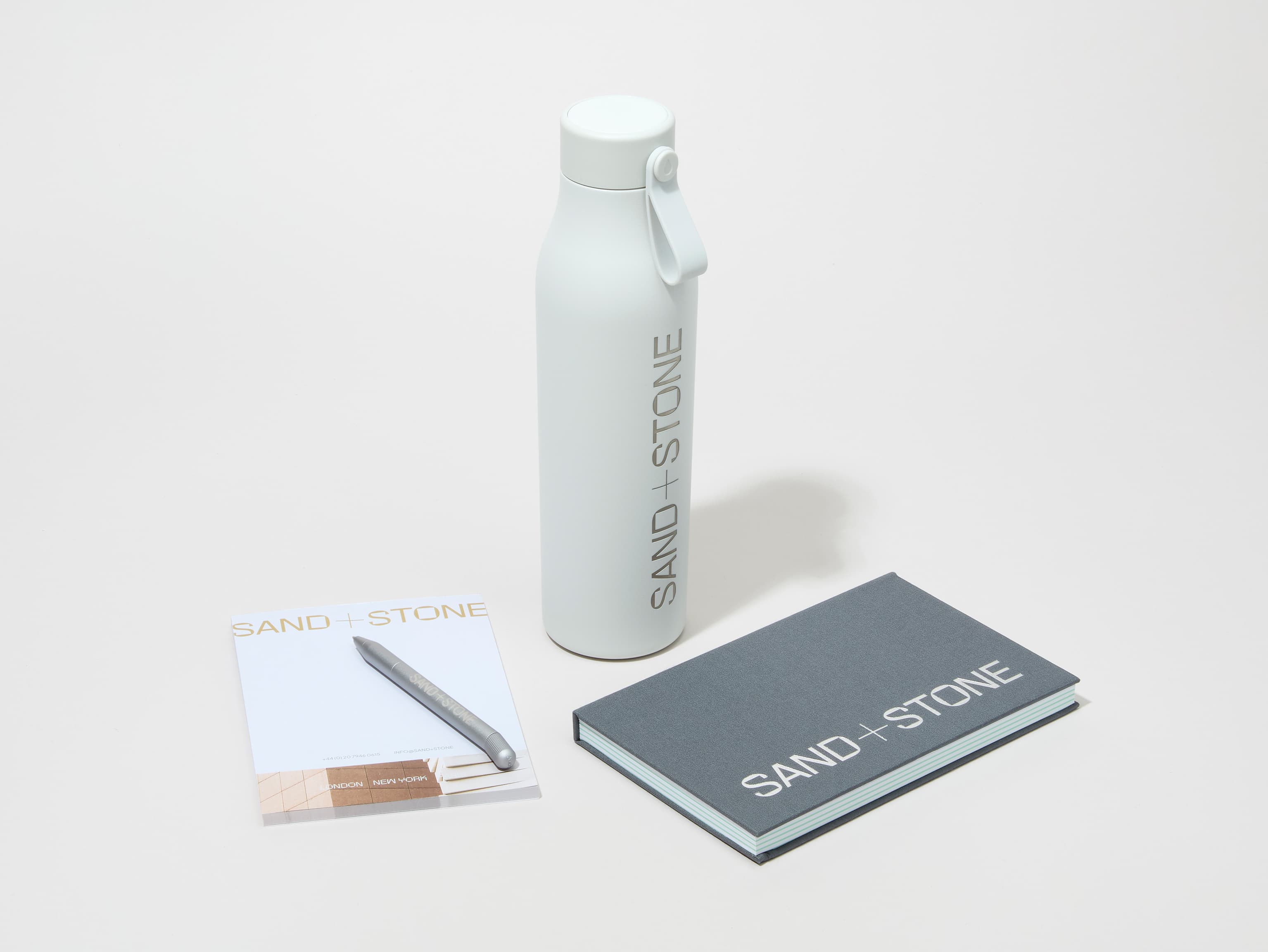 A collection image of a cloudy grey MOO water bottle with custom engraving alongside a notebook, notepad and pen.