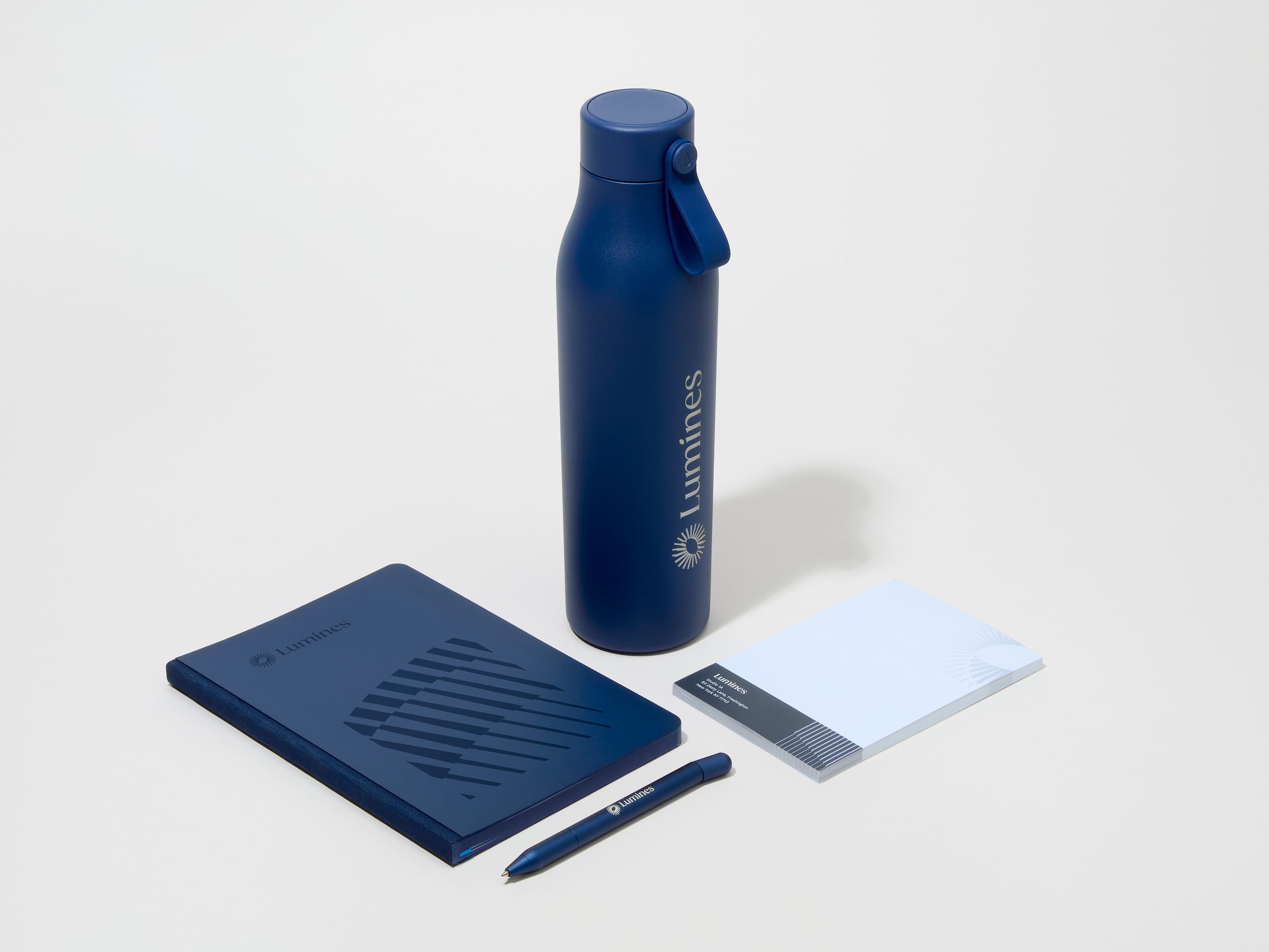 A collection image of a midnight blue MOO water bottle with custom engraving alongside a notebook, notepad and pen.