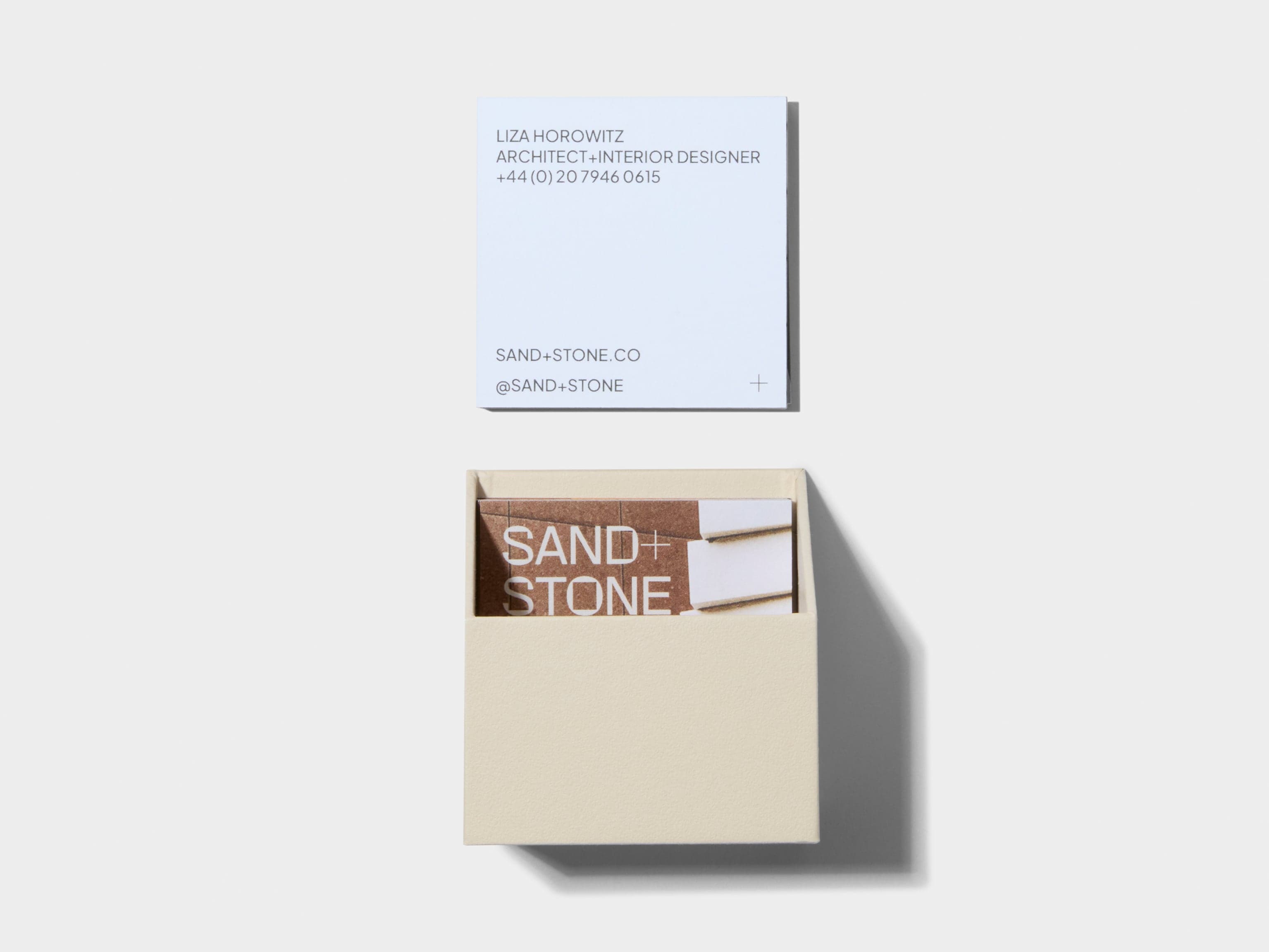 An open off white square business card box with customised luxe business cards placed inside and above the box.