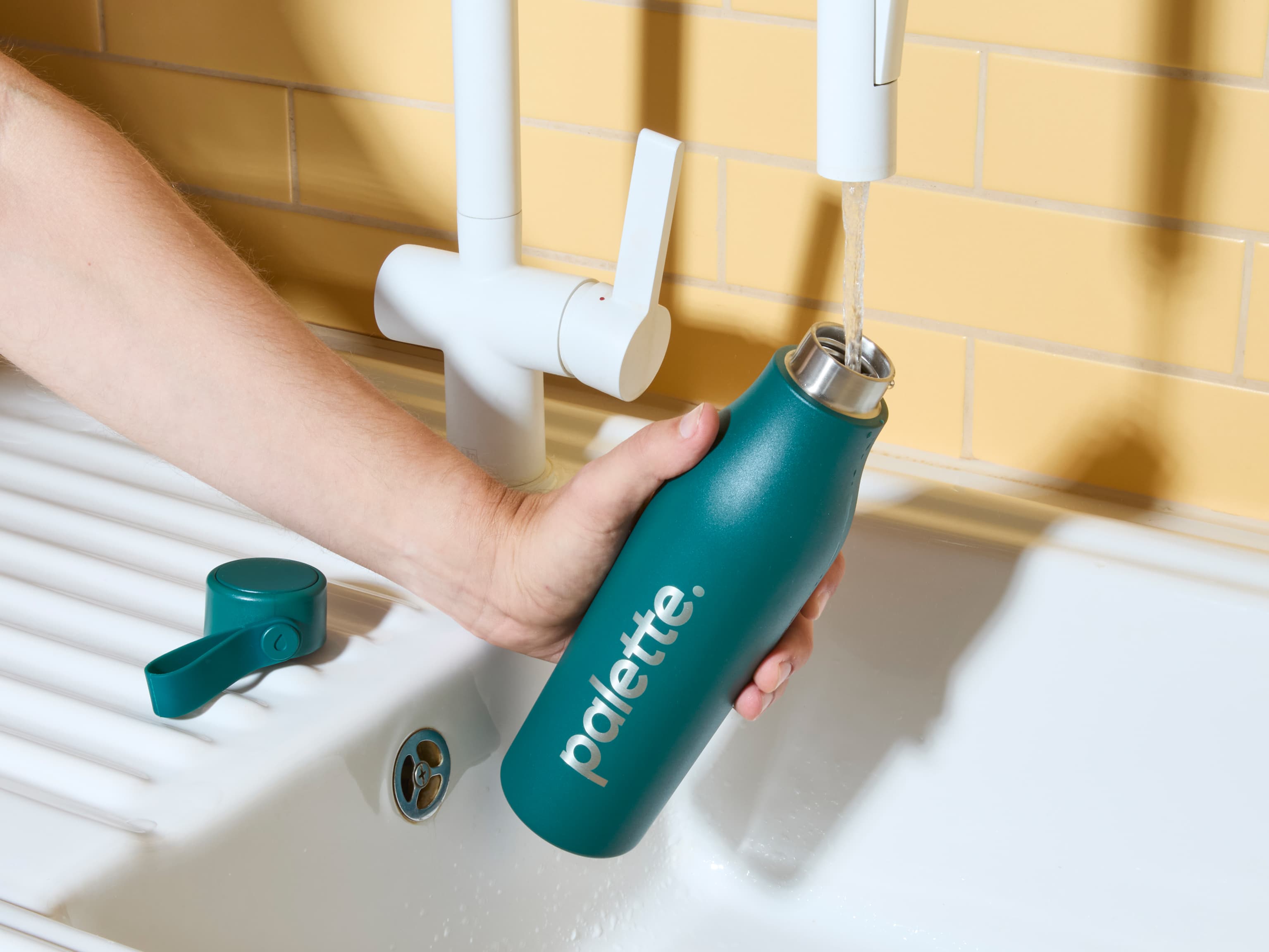 Someone filling a custom green water bottle from a tap.