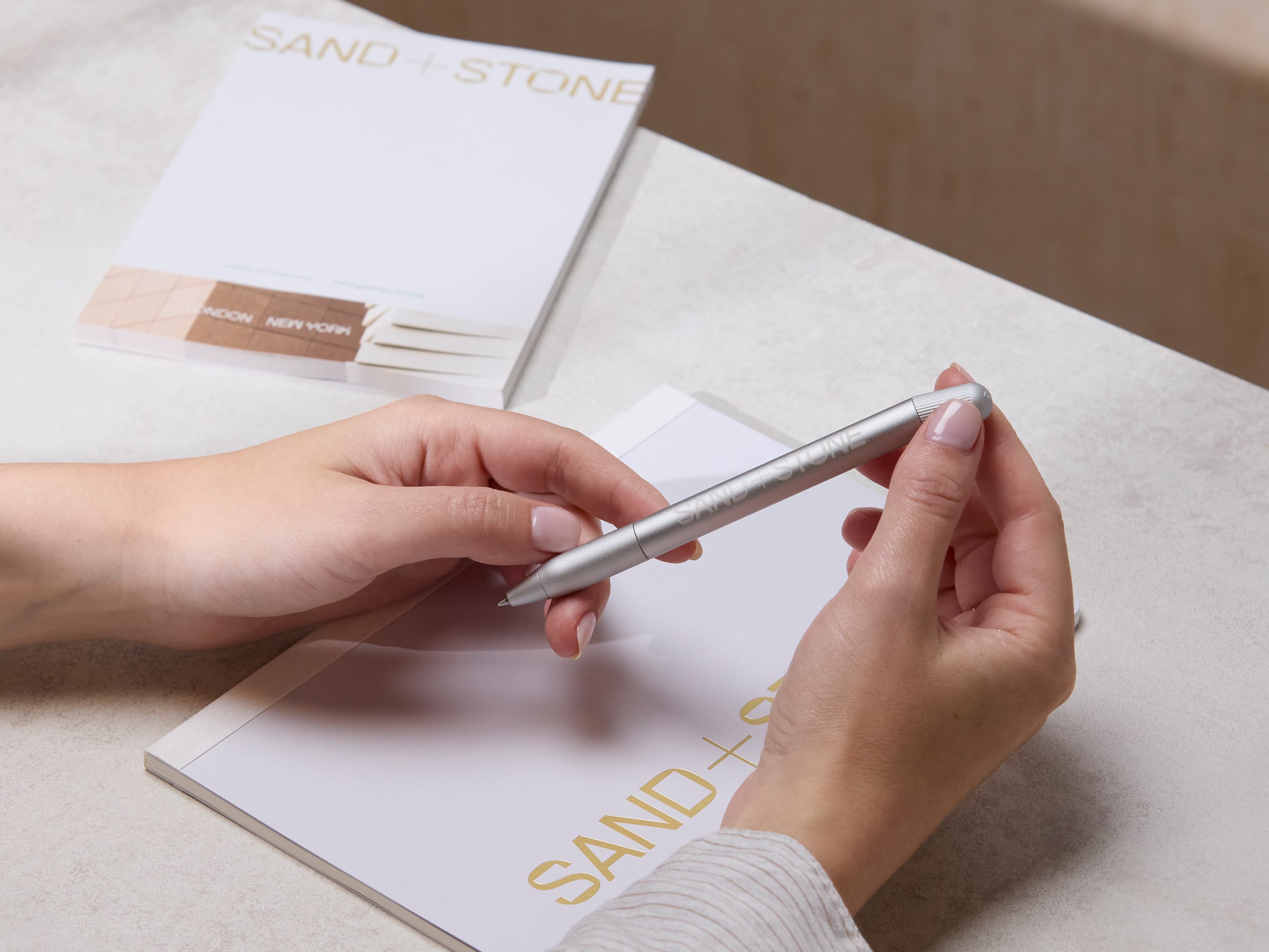 A person holding a custom aluminium pen with white branding.