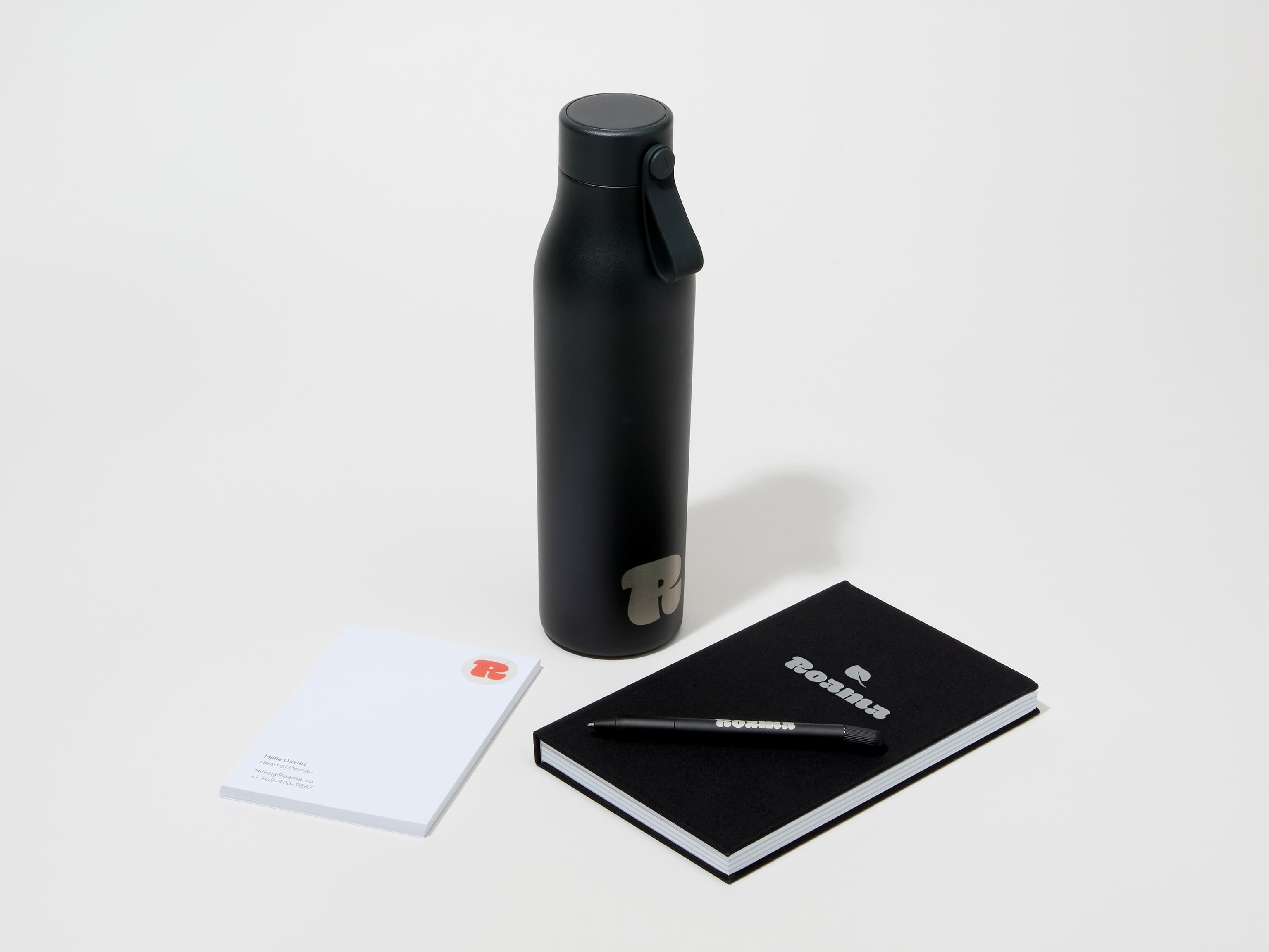 A collection image of a jet black MOO water bottle with custom engraving alongside a notebook, notepad and pen.