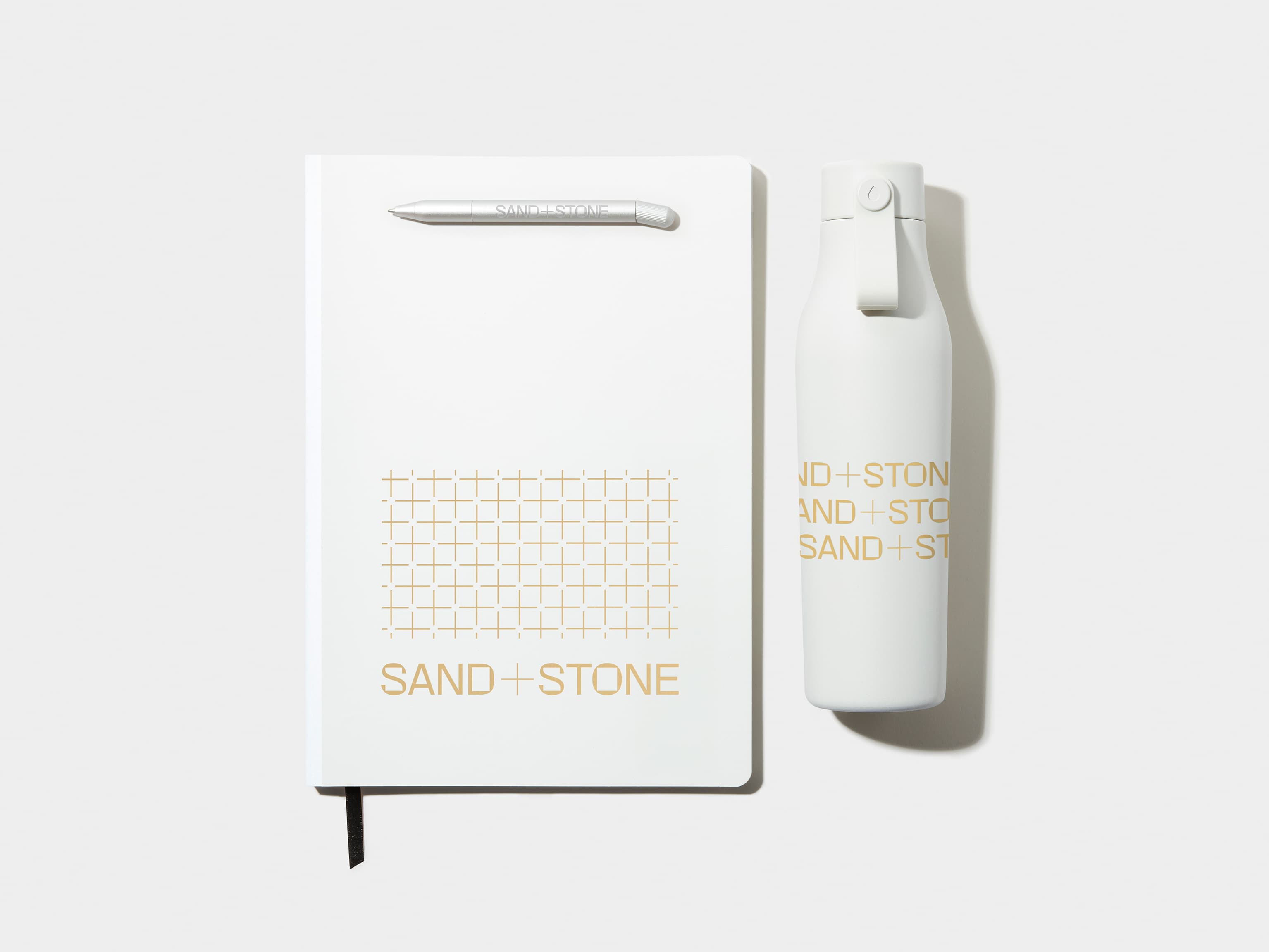 A large cloudy grey notebook with gold foil customisation alongside a custom cloudy grey pen and water bottle.