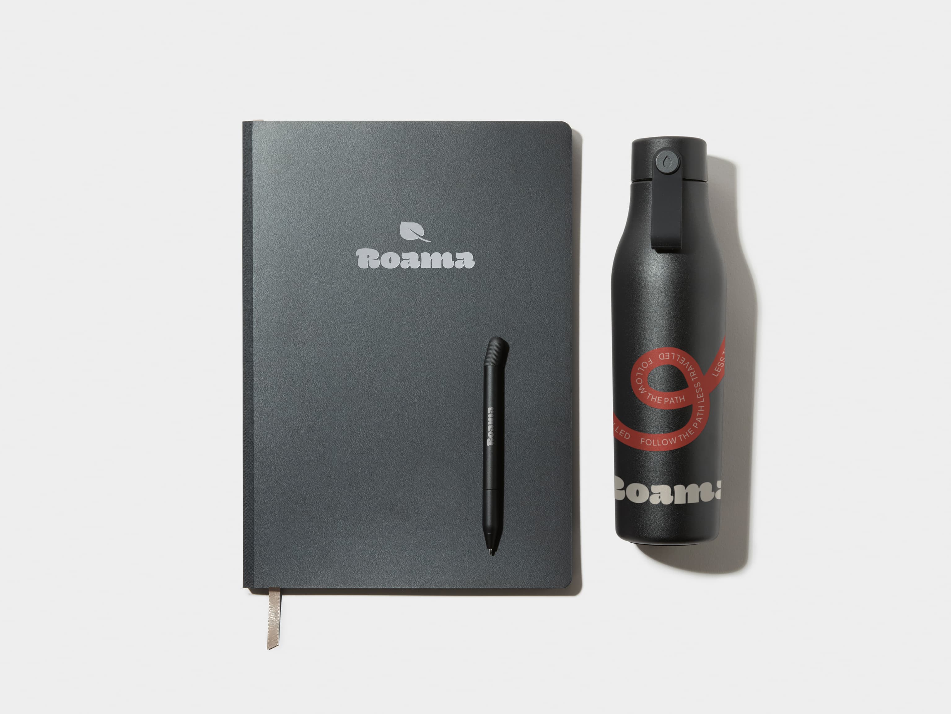 A large jet black softcover notebook with silver foil customisation, alongside a black custom pen and water bottle.