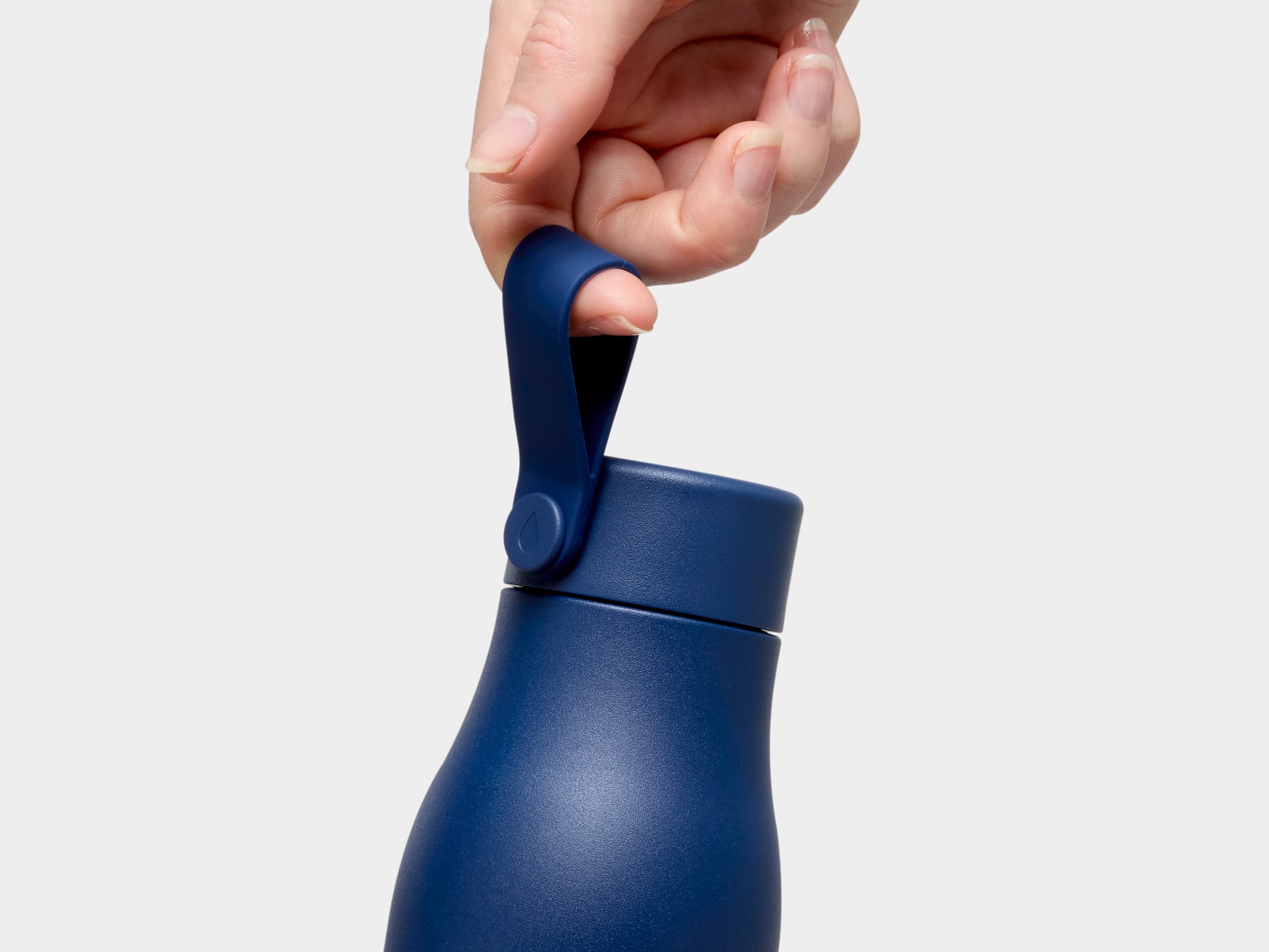 A close up of a person holding a midnight blue MOO water bottle by the top strap.
