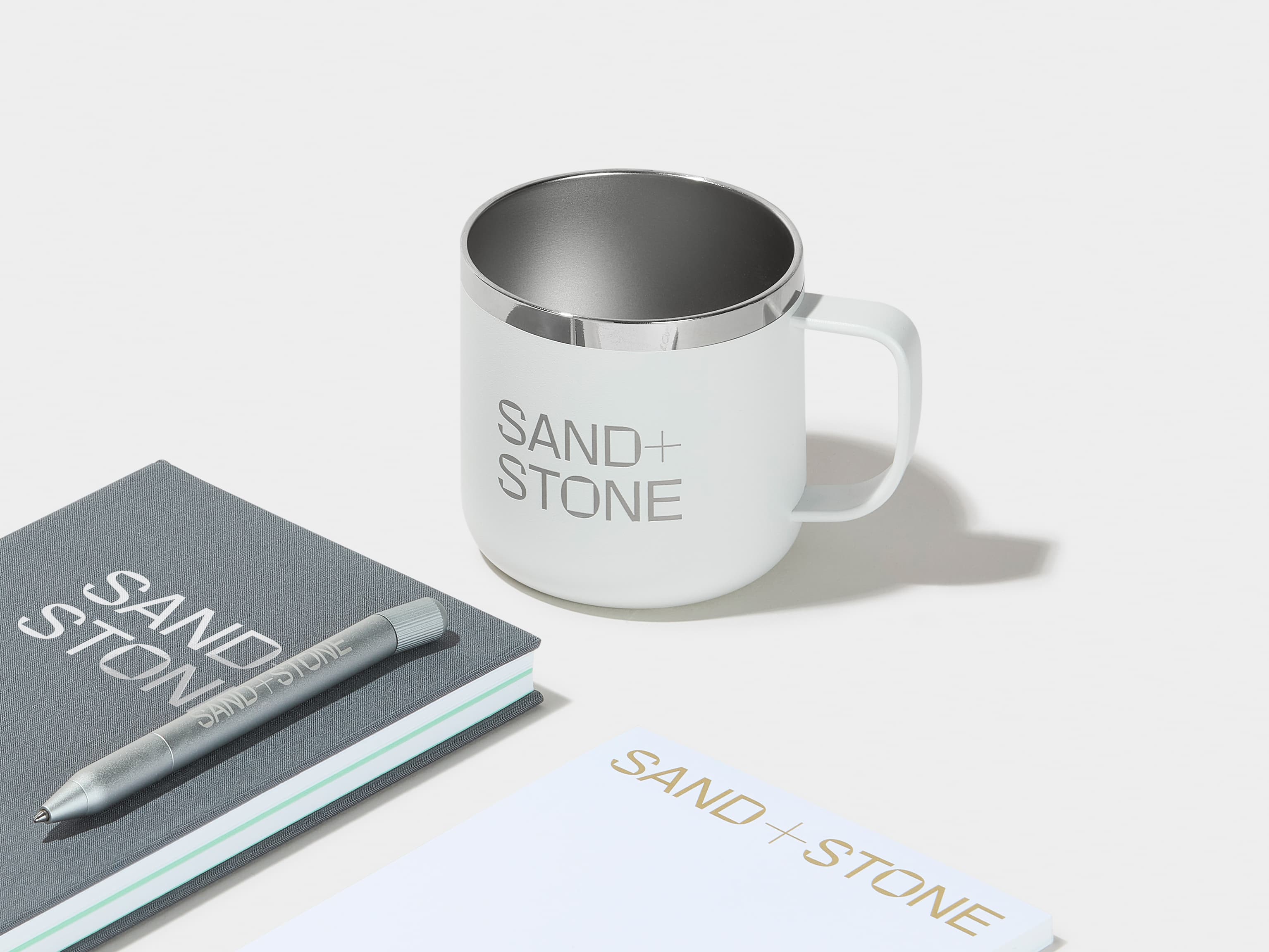 A collection of cloudy grey and white branded merchandise including a insulated mug, notebook and pen.