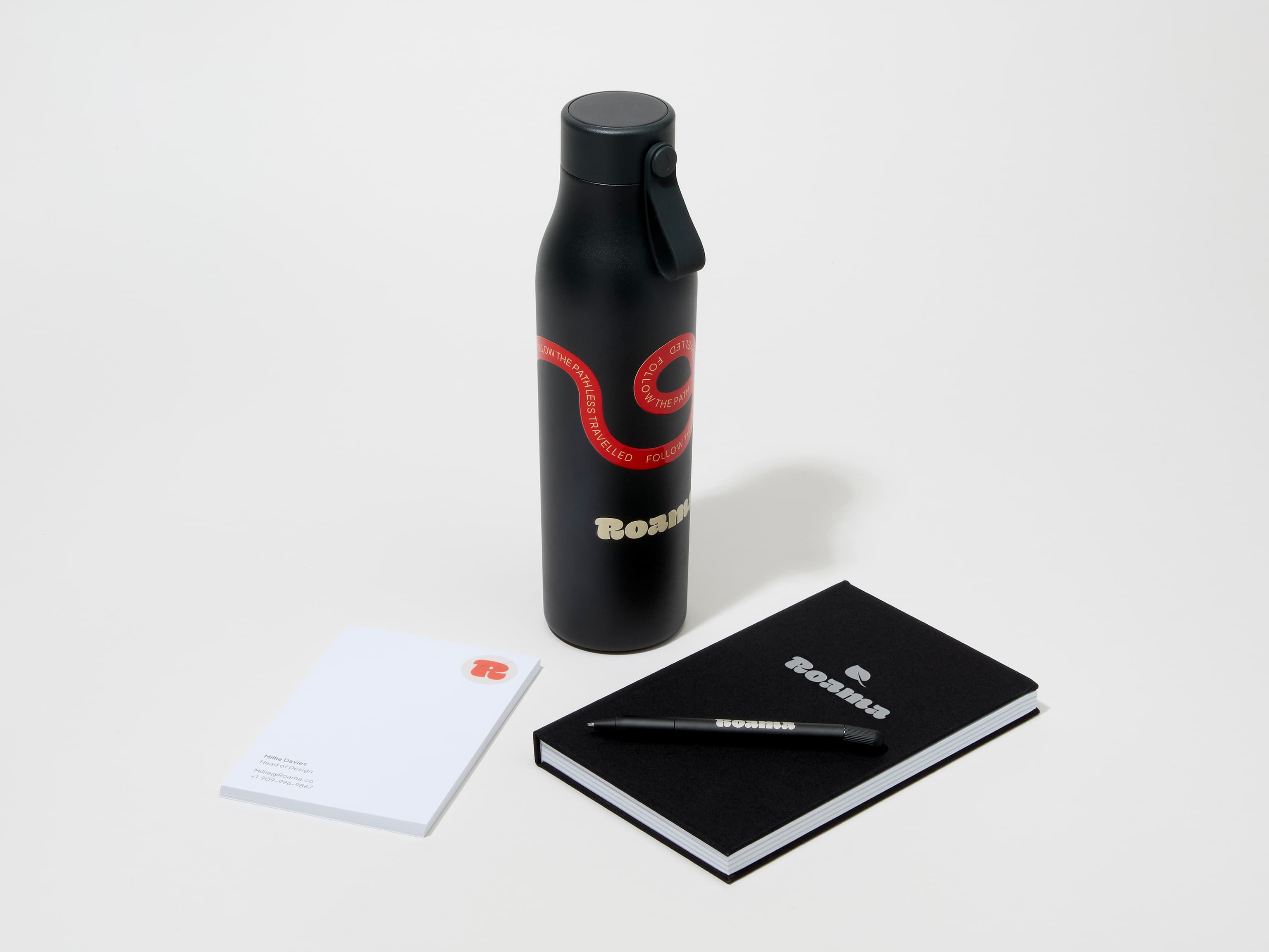 A collection image of a jet black MOO water bottle with custom 360 wrap printing alongside a notebook, notepad and pen.