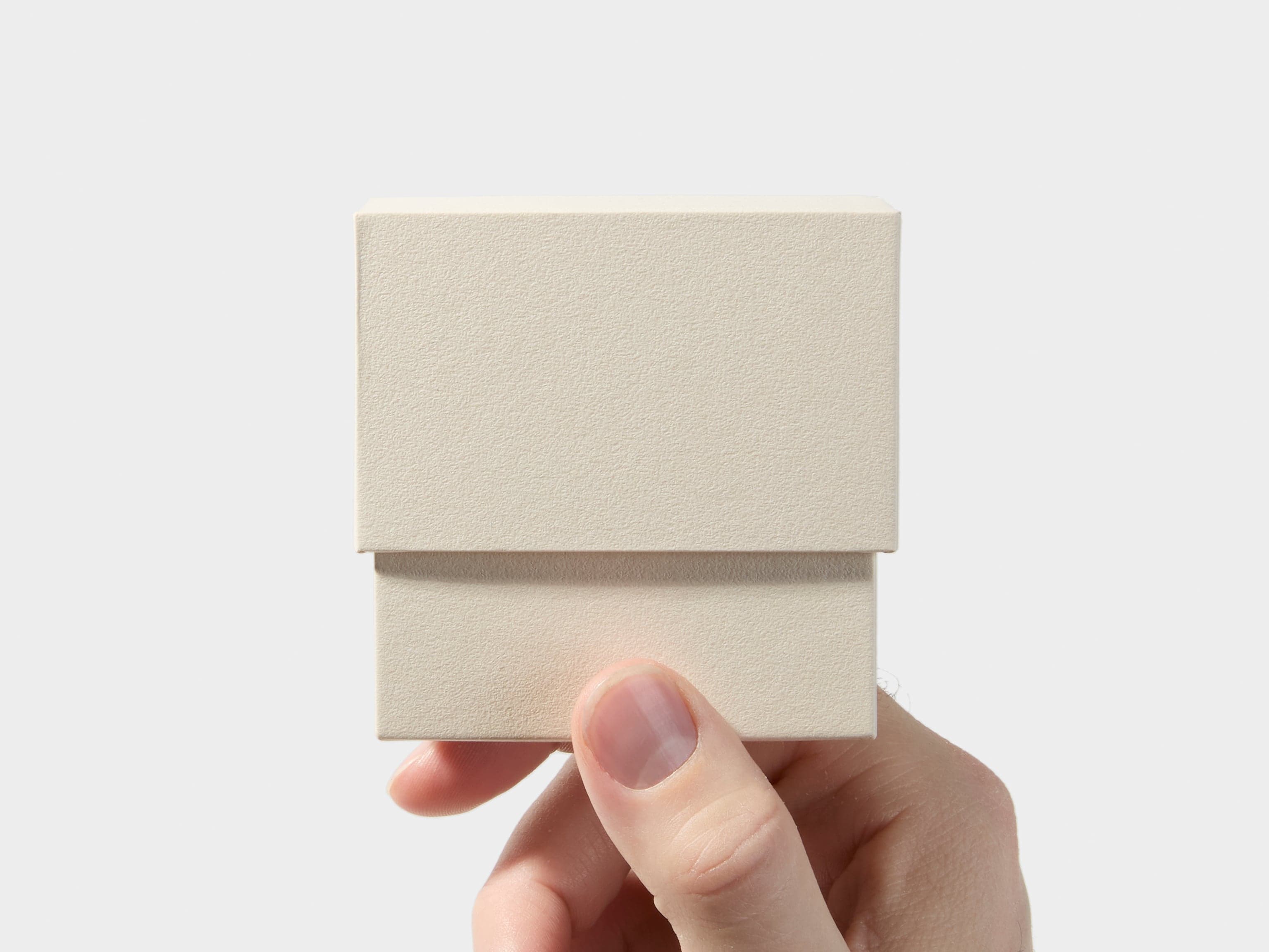 A hand holding an off white square business card box.