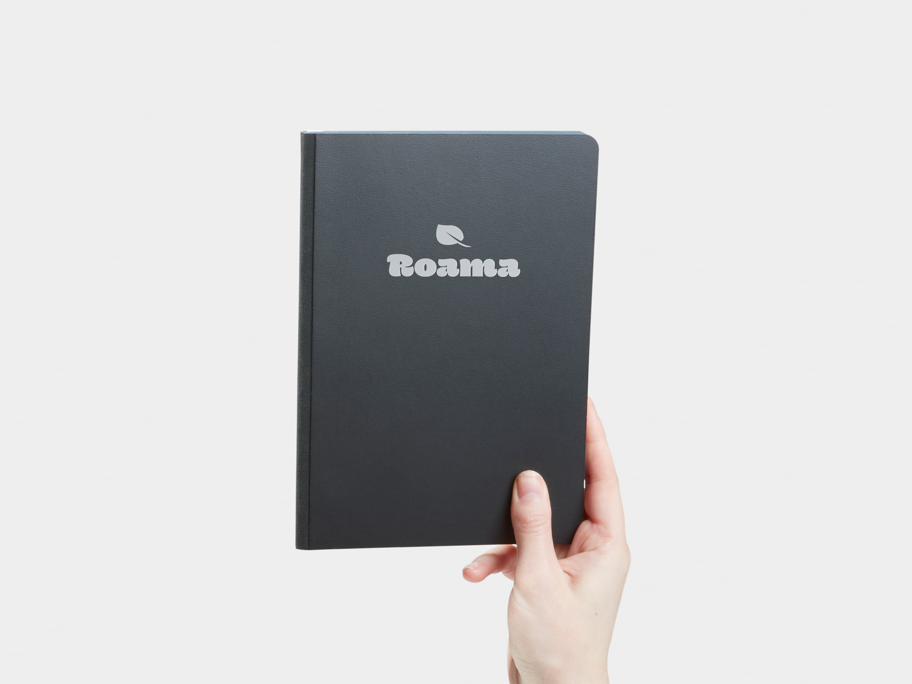 A hand holding a jet black softcover notebook with silver foil customisation.