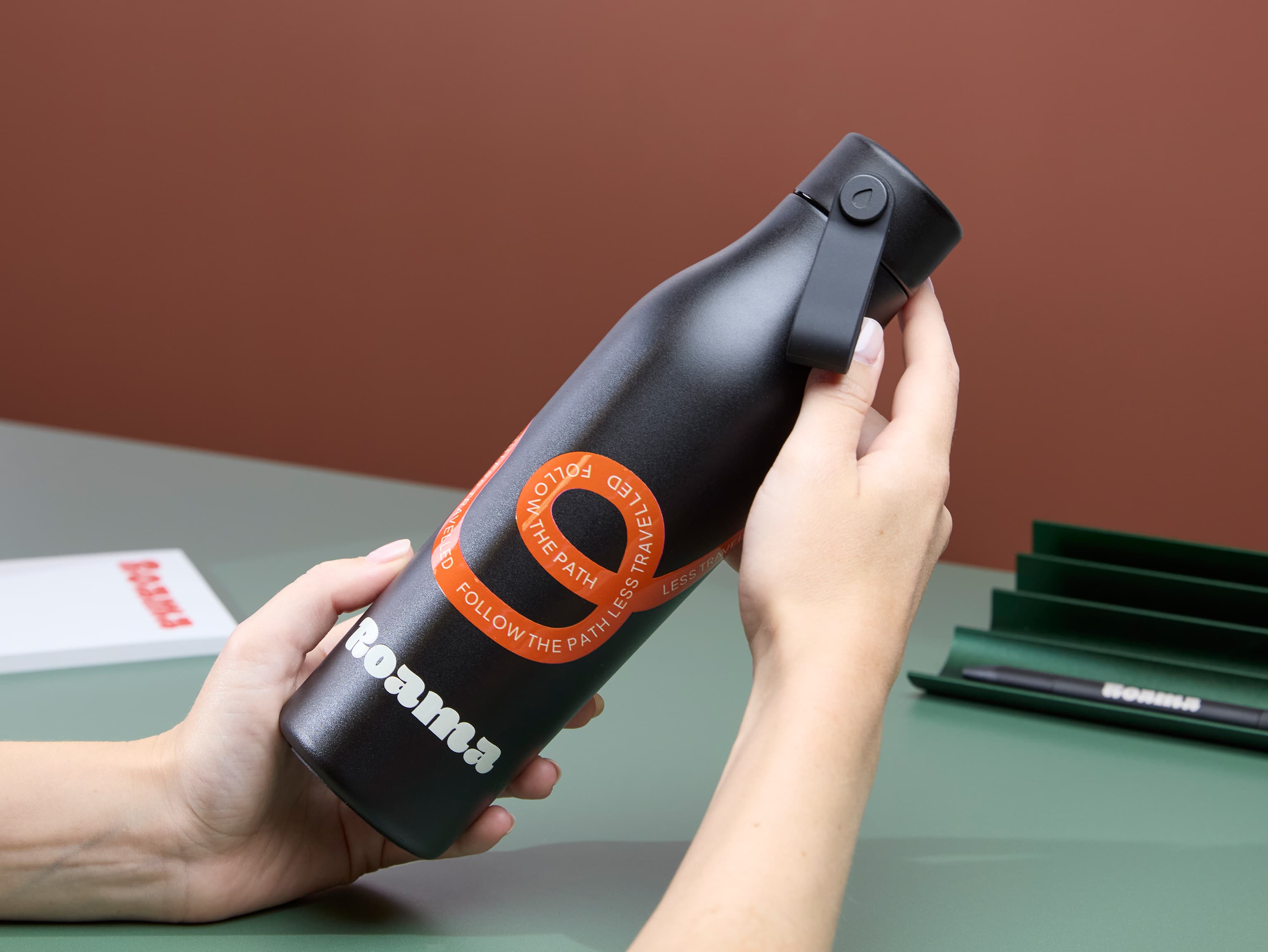 A person holding a jet black water bottle with custom branding.