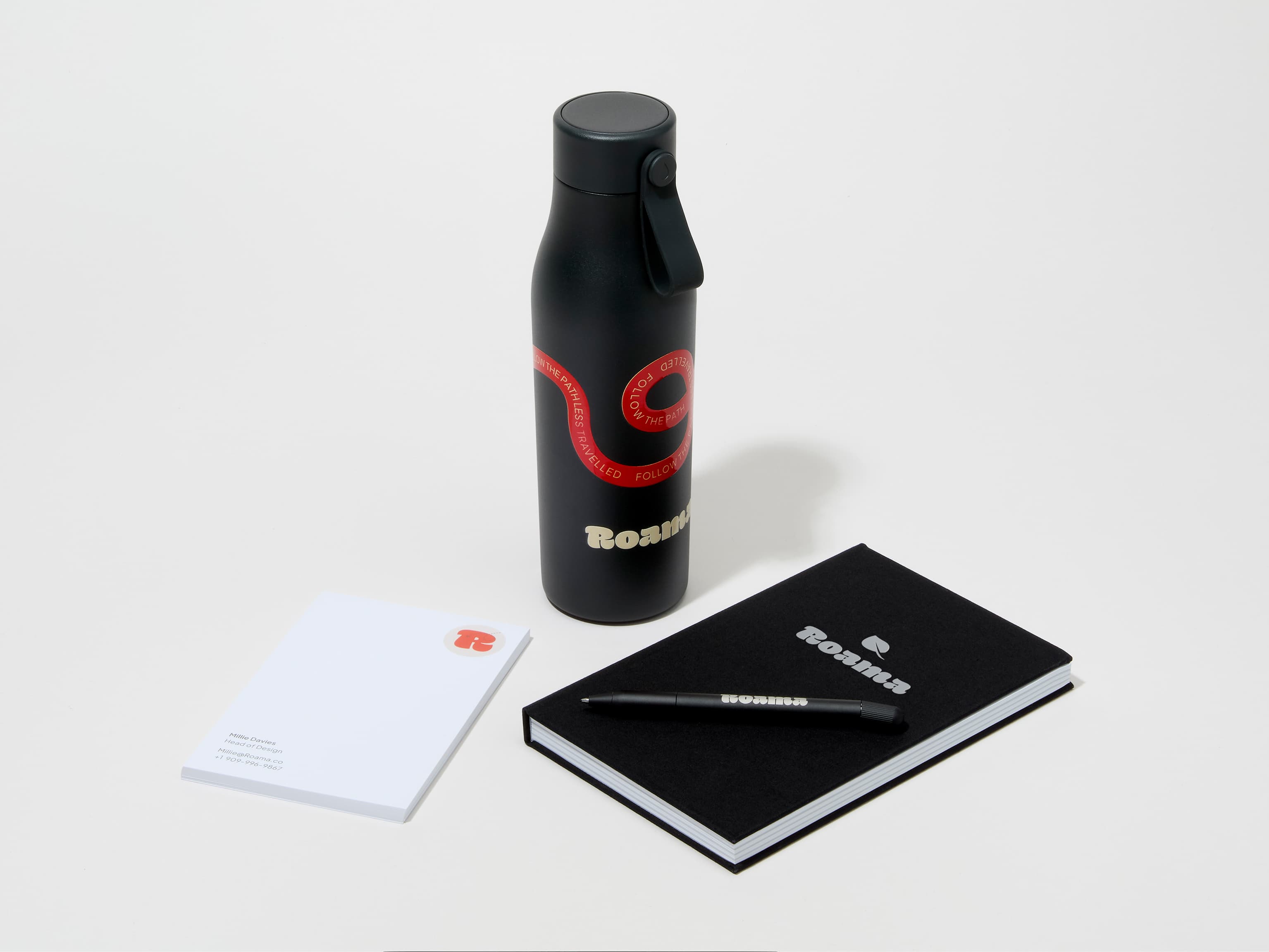 A collection of branded merchandise including a jet black MOO water bottle with customized 360 wrap printing alongside a notepad, notebook and pen.