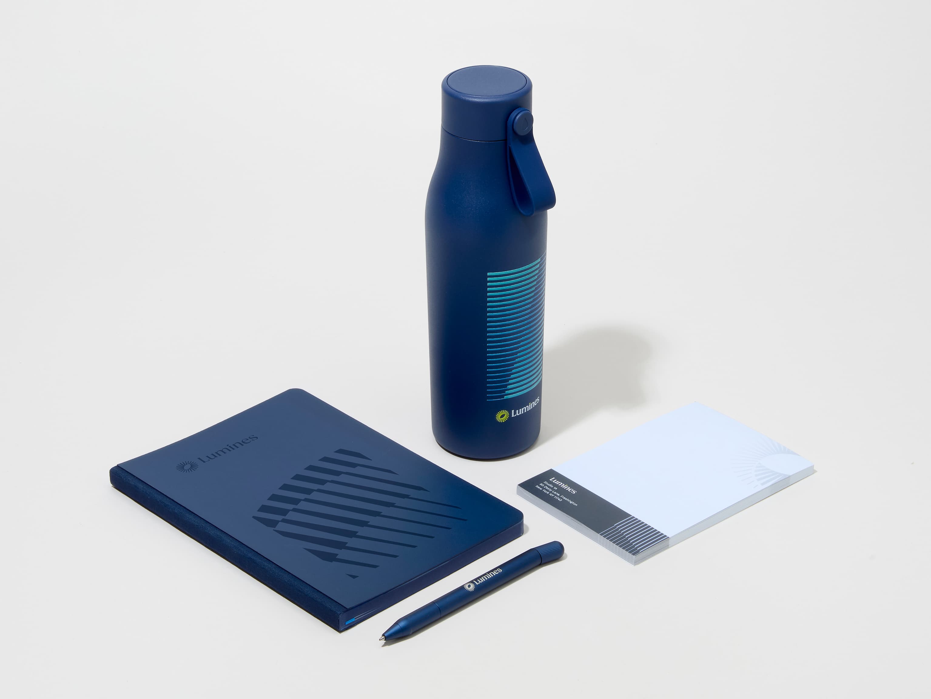 A collection of branded merchandise including a midnight blue MOO water bottle with customized printing alongside a notepad, notebook and pen.