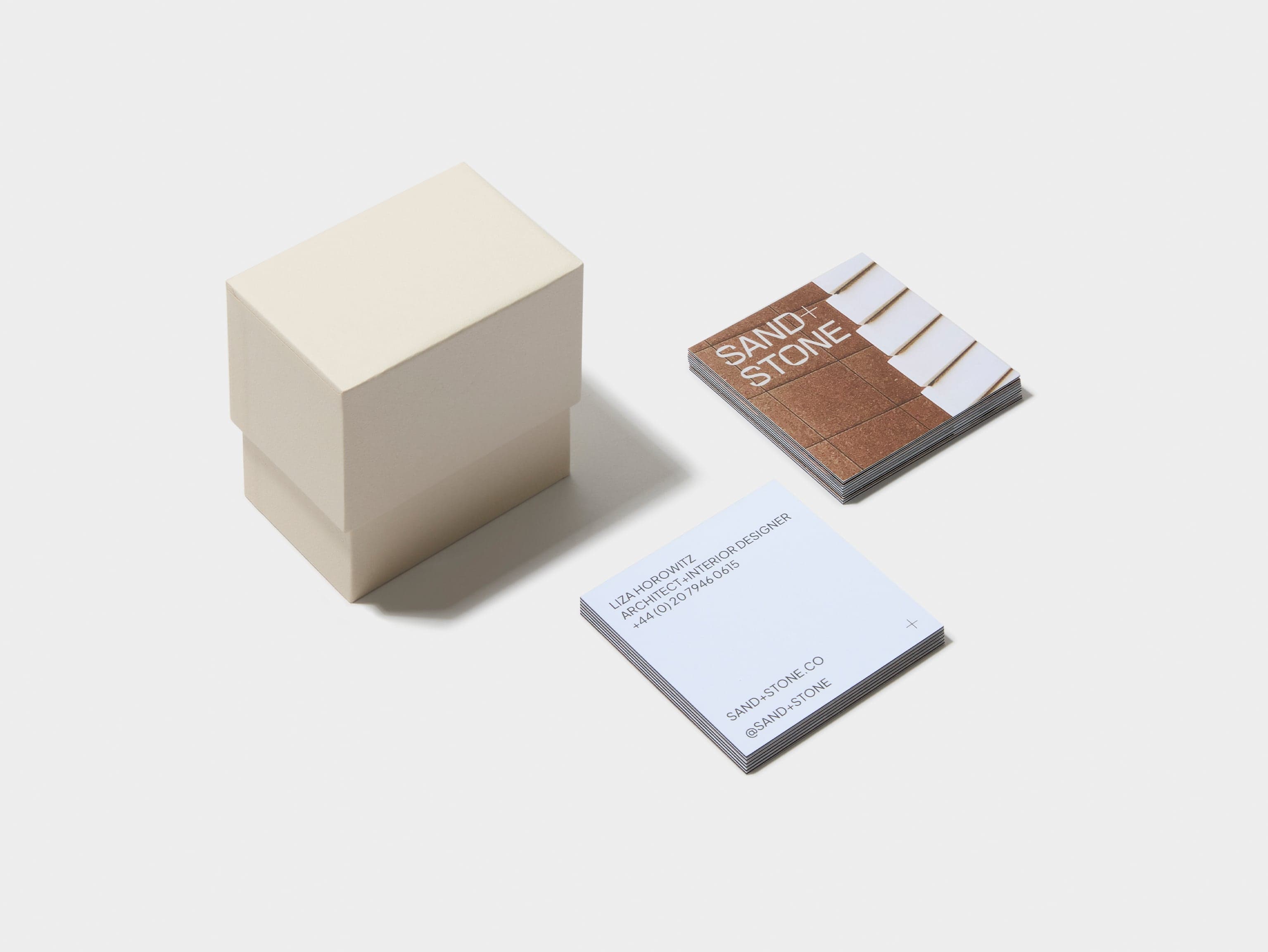 A square off white business card box placed alongside two piles of customised luxe business cards.