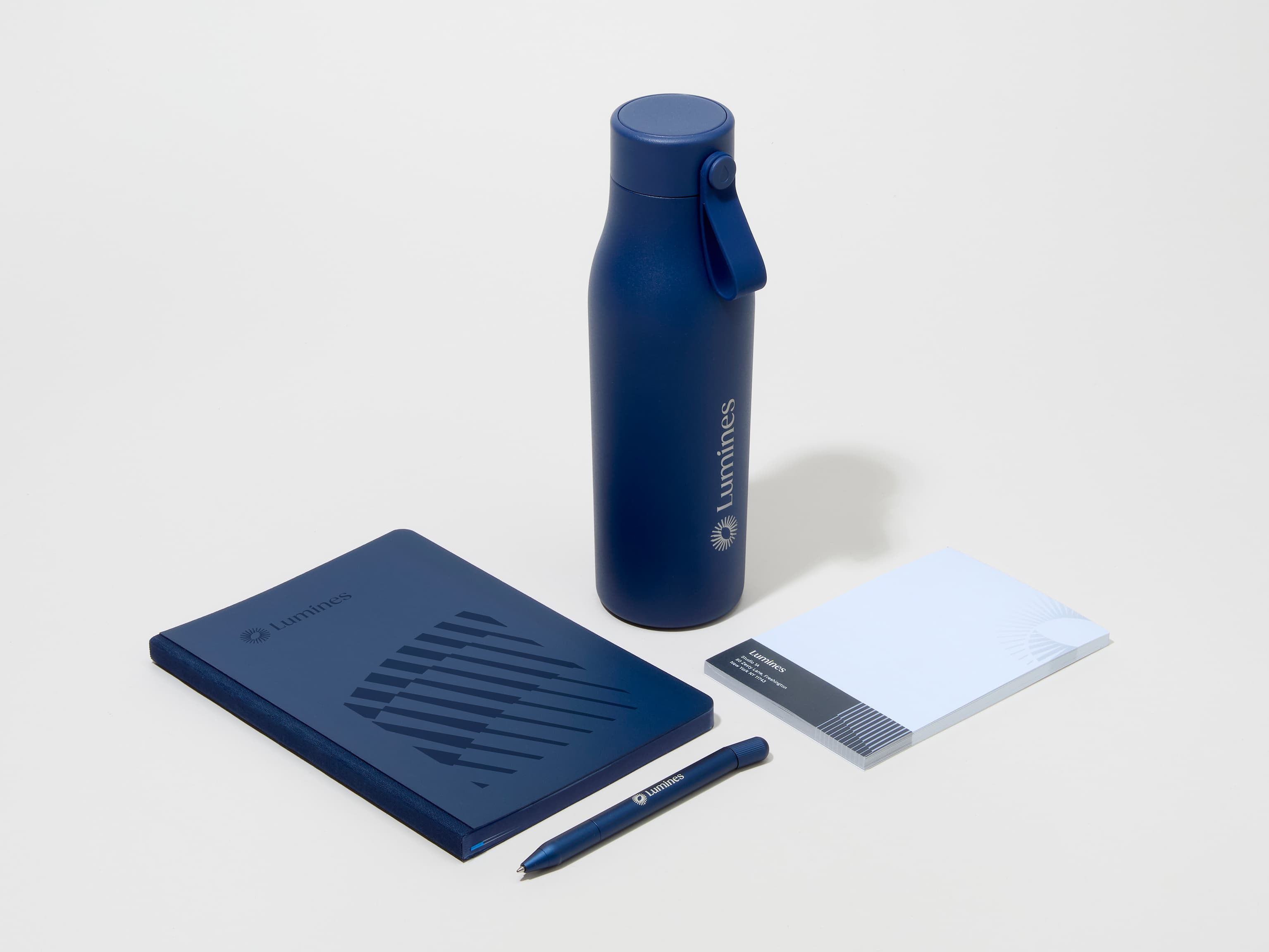 A collection of branded merchandise including a midnight blue MOO water bottle with customized engraving alongside a notepad, notebook and pen.