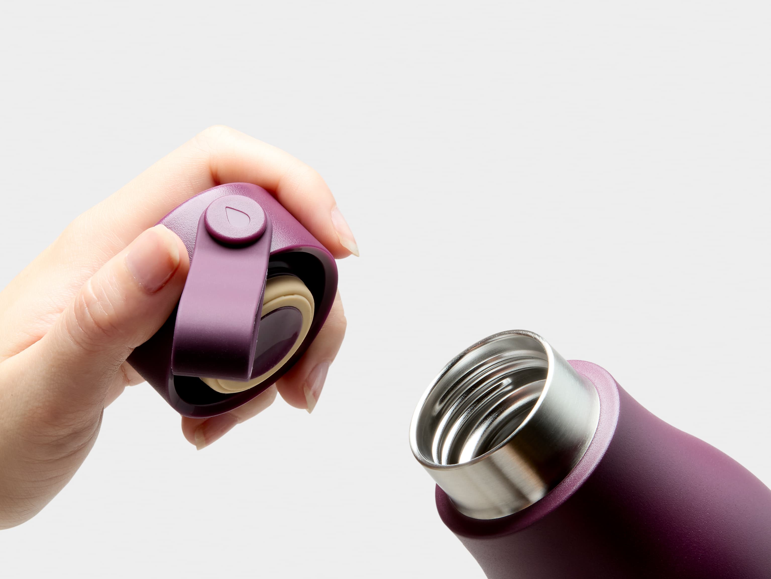 A close up image of the mouth and a hand holding the lid of a mulberry MOO water bottle.