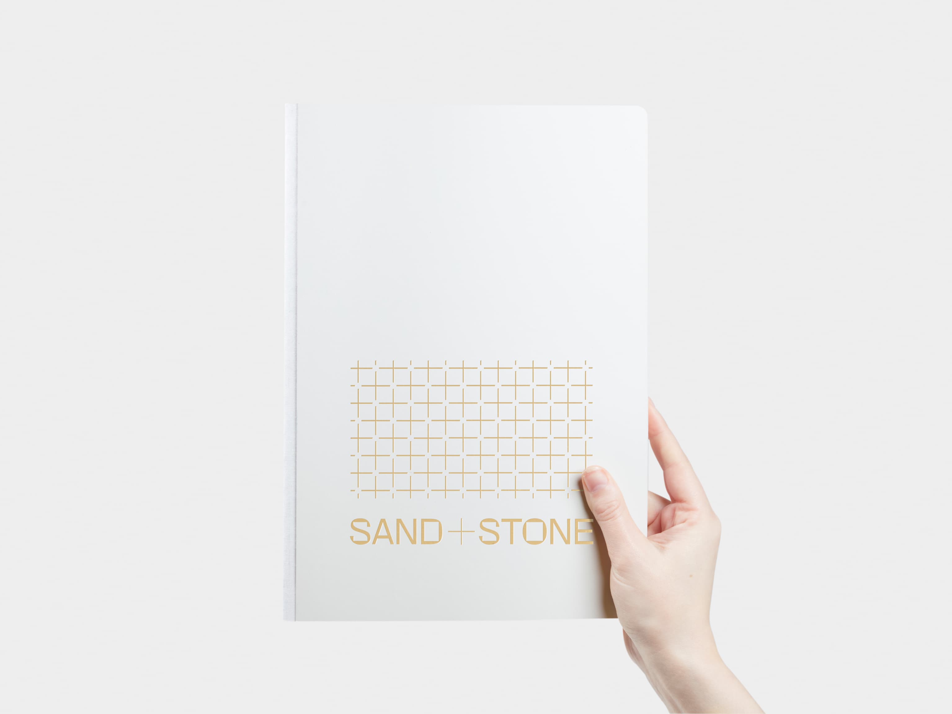 A hand holding a large cloudy grey softcover notebook with gold foil customisation.