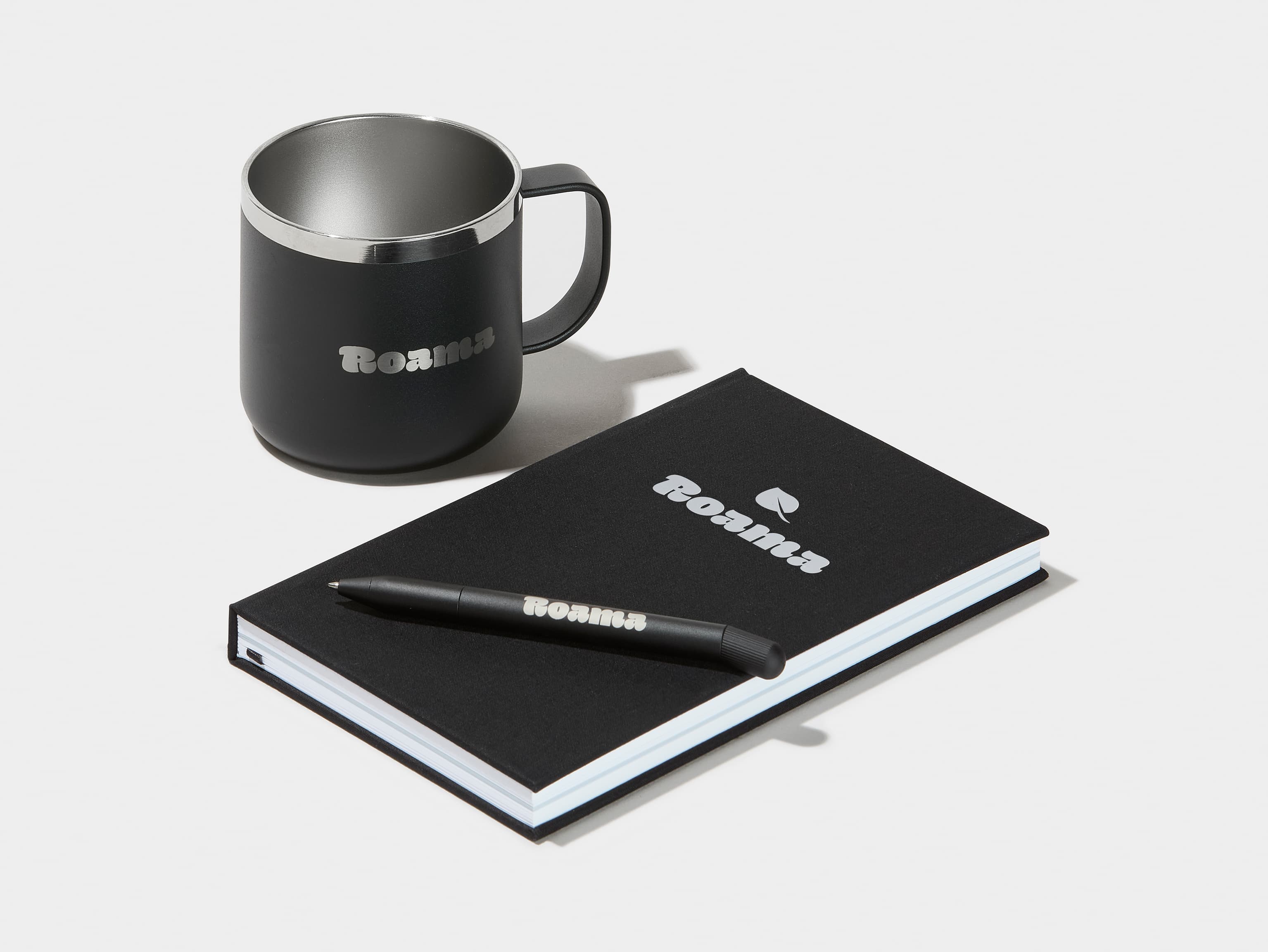 A collection of black branded merchandise including a insulated mug, notebook and pen.