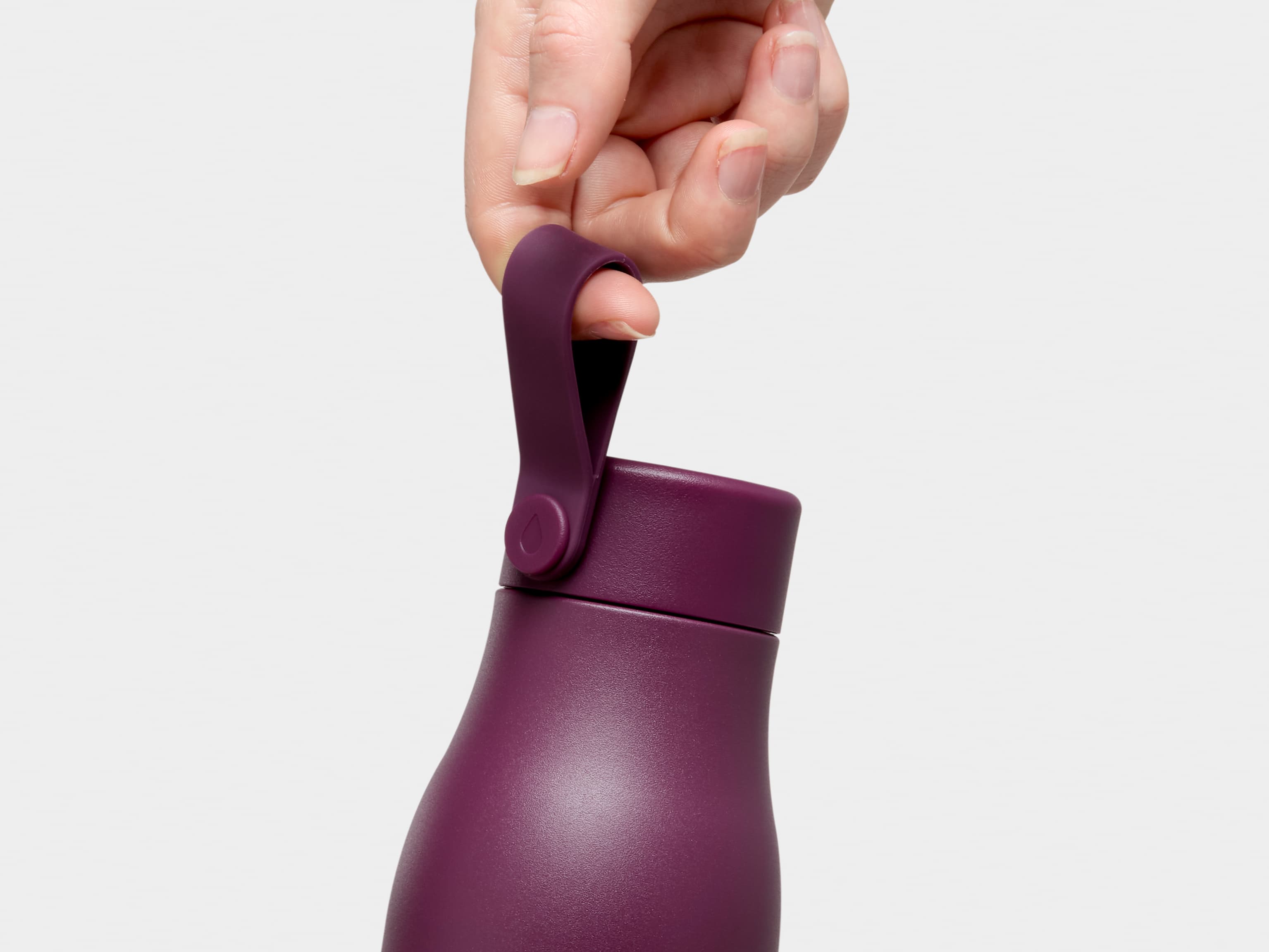 A close up of a person holding a mulberry MOO water bottle by the top strap.