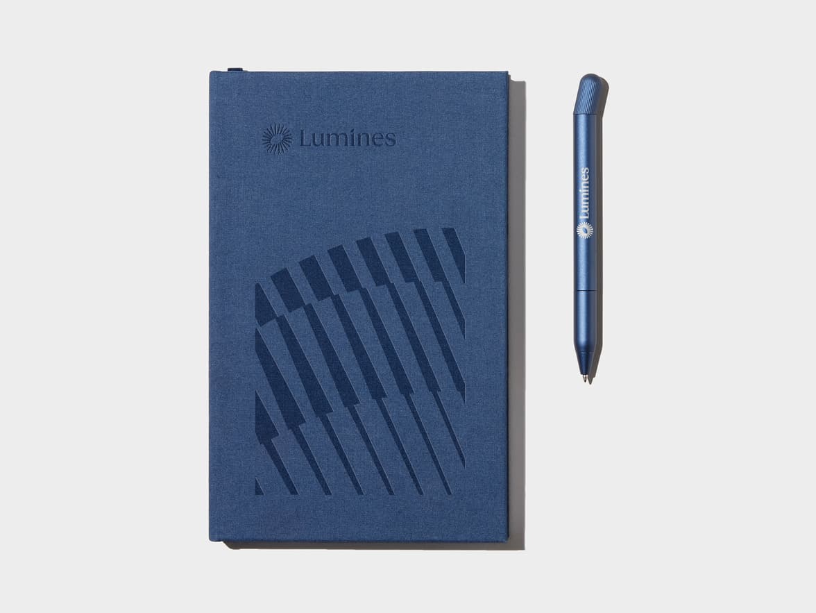 A custom blue pen beside a custom blue notebook.