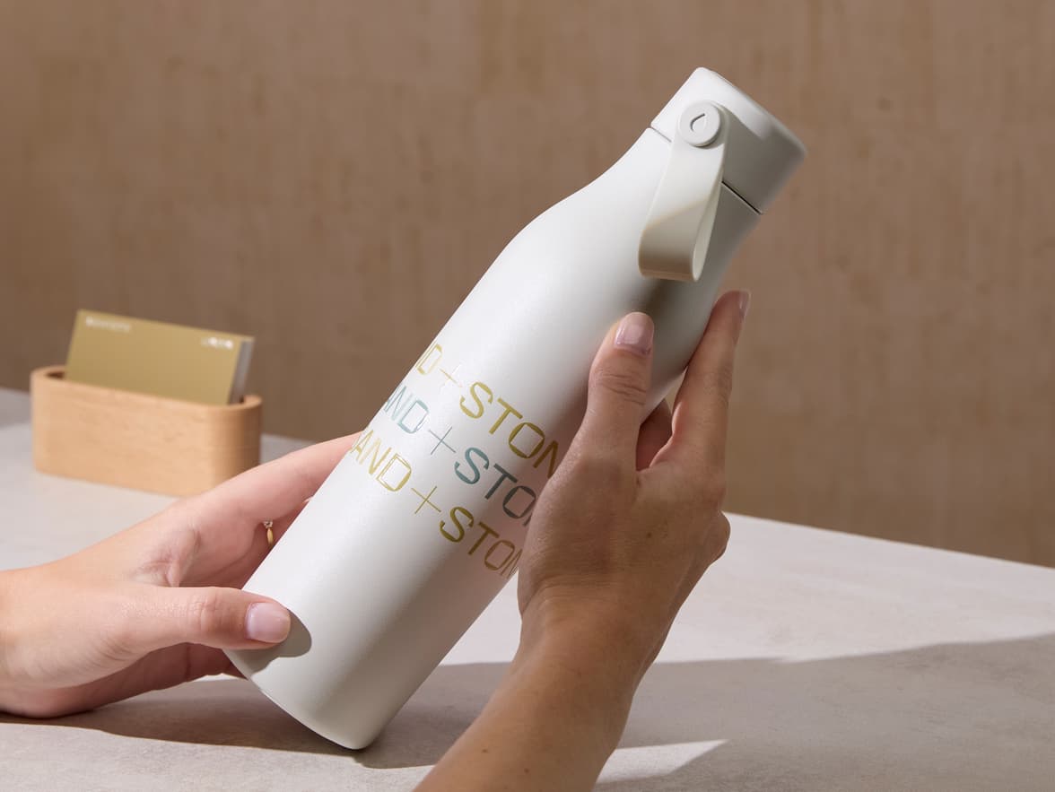 Person holding a custom cloud grey water bottle with gold and blue branding.