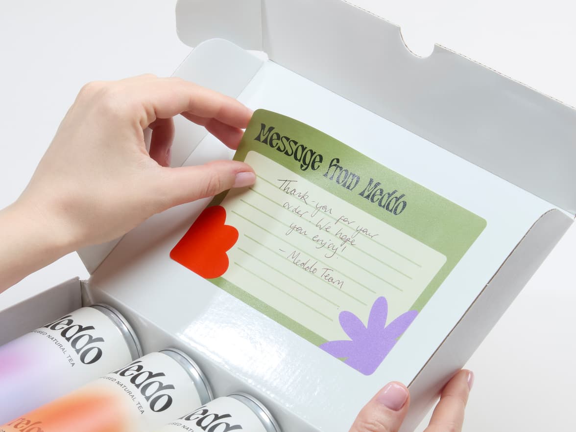 A person placing a customized matte paper sticker in size 6x4 inside a cardboard box packaging.