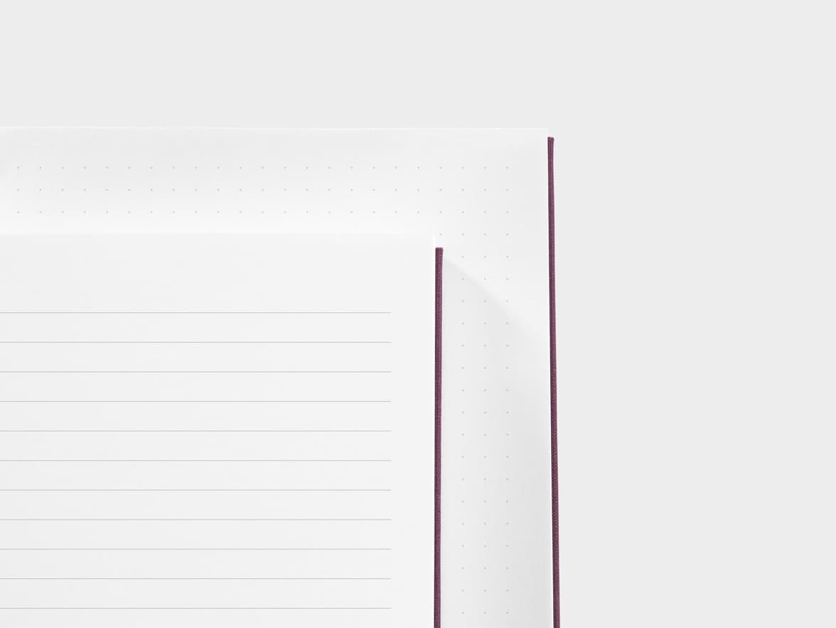 A detail image of the top corner of two hardcover notebooks placed on top of each other, displaying the difference in lined and dotted white pages.