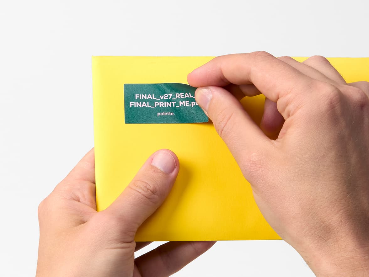 Hands placing a green and purple customized rectangular coated sticker onto a yellow envelope.
