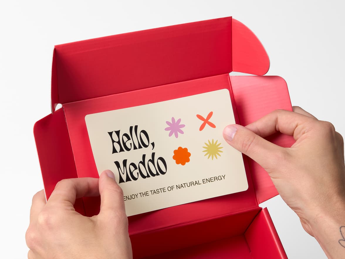 Hands placing a large customized coated rectangular sticker into a red packaging box.