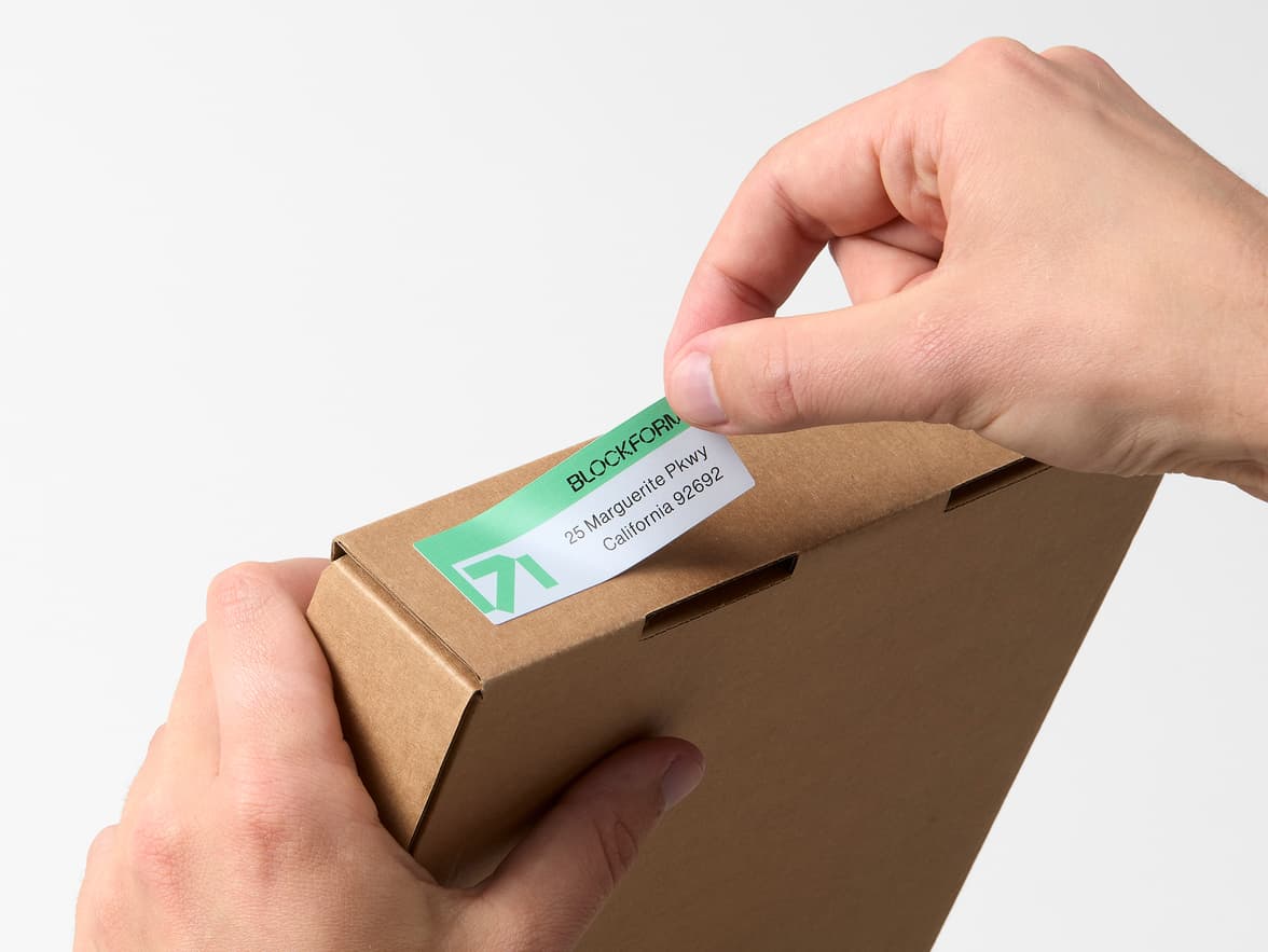 Hands placing a customized rectangular coated sticker onto a cardboard box.